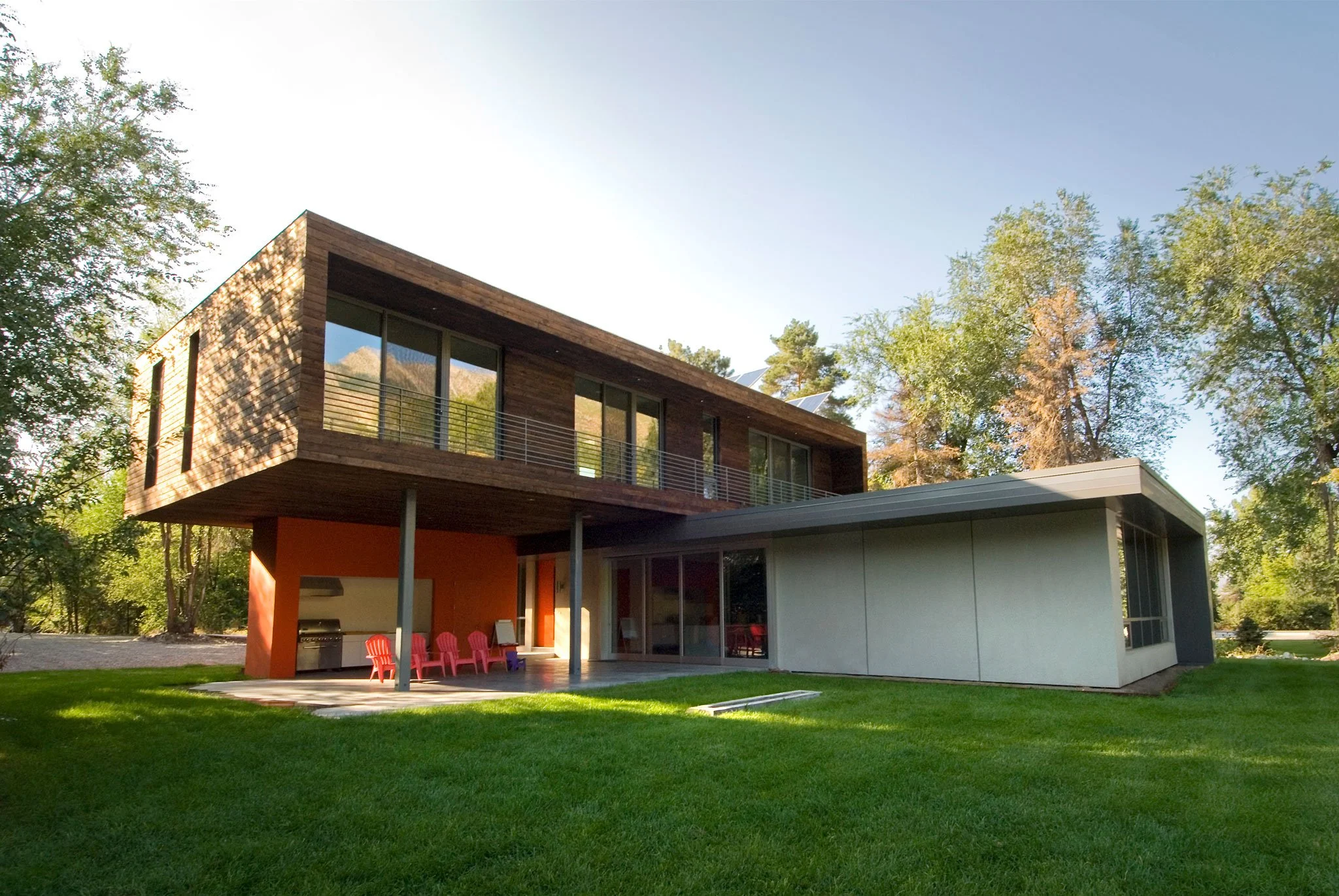 Modern off-grid home with a cantilevered upper volume in wood and a green lawn, Johnson, Holladay, Utah.