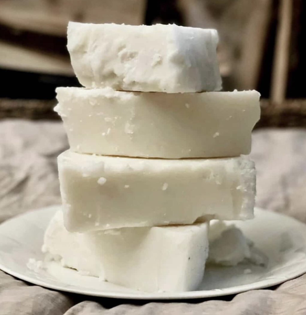 A stack of four blocks of white cheese on a white plate, with a blurred background.