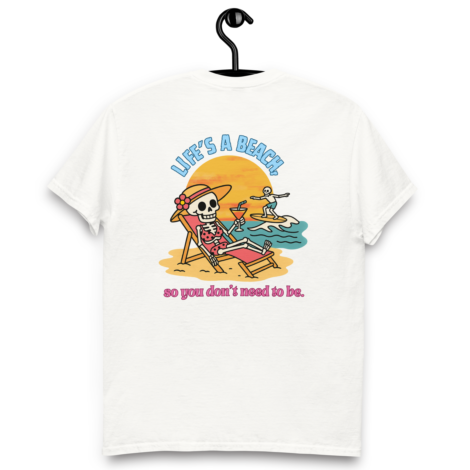 A white T-shirt hanging on a black hook, featuring a colorful illustration of a skeleton woman relaxing on a beach chair with a drink, and a smaller skeleton surfing in the water at sunset. Text reads "Life's a beach so you don't need to be."