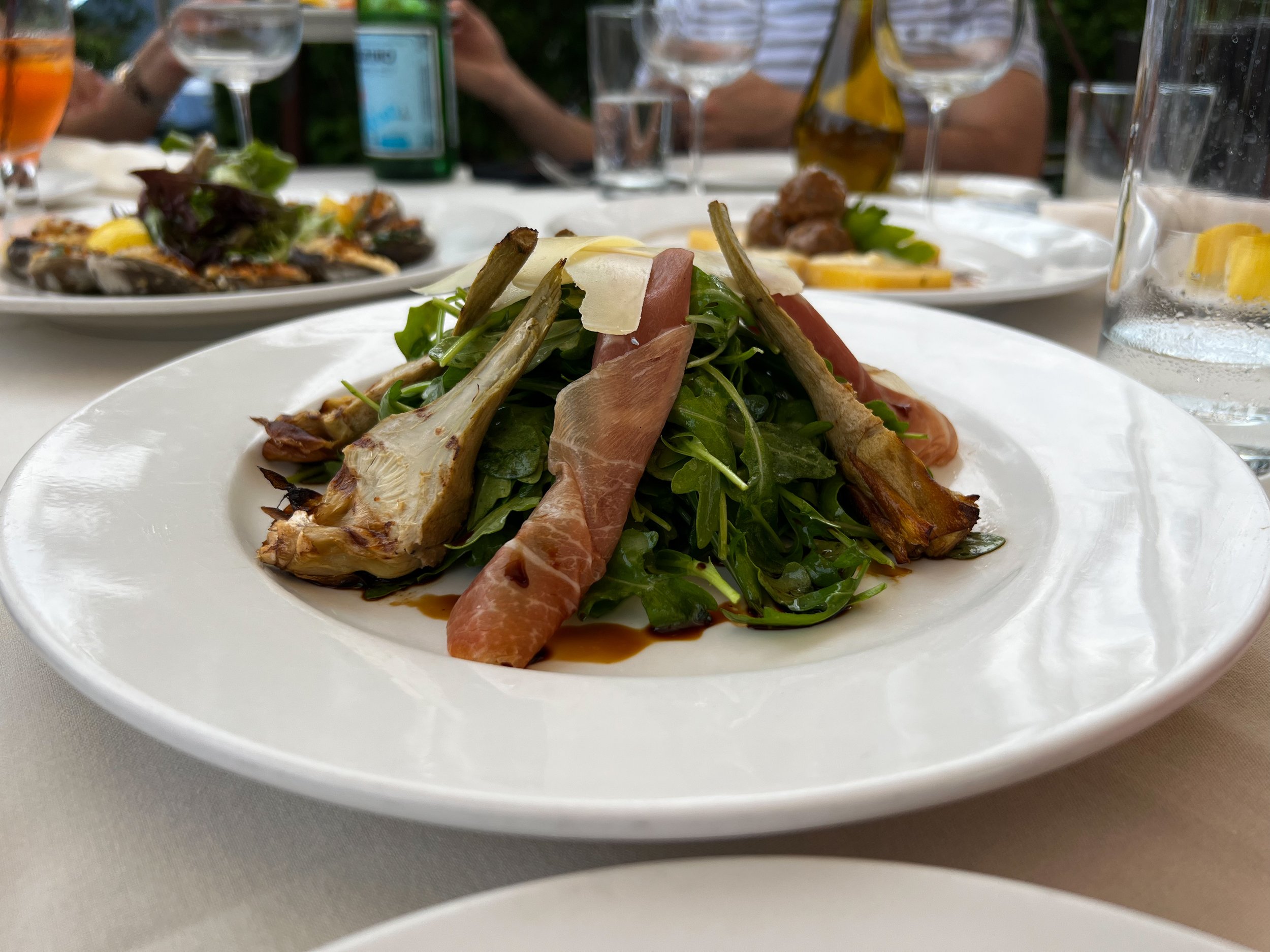Prosciutto wrapped char grilled Artichoke hearts on a bed of arugula and topped with sliced Parmigiano Reggiano, oil and balsamic vinegar.