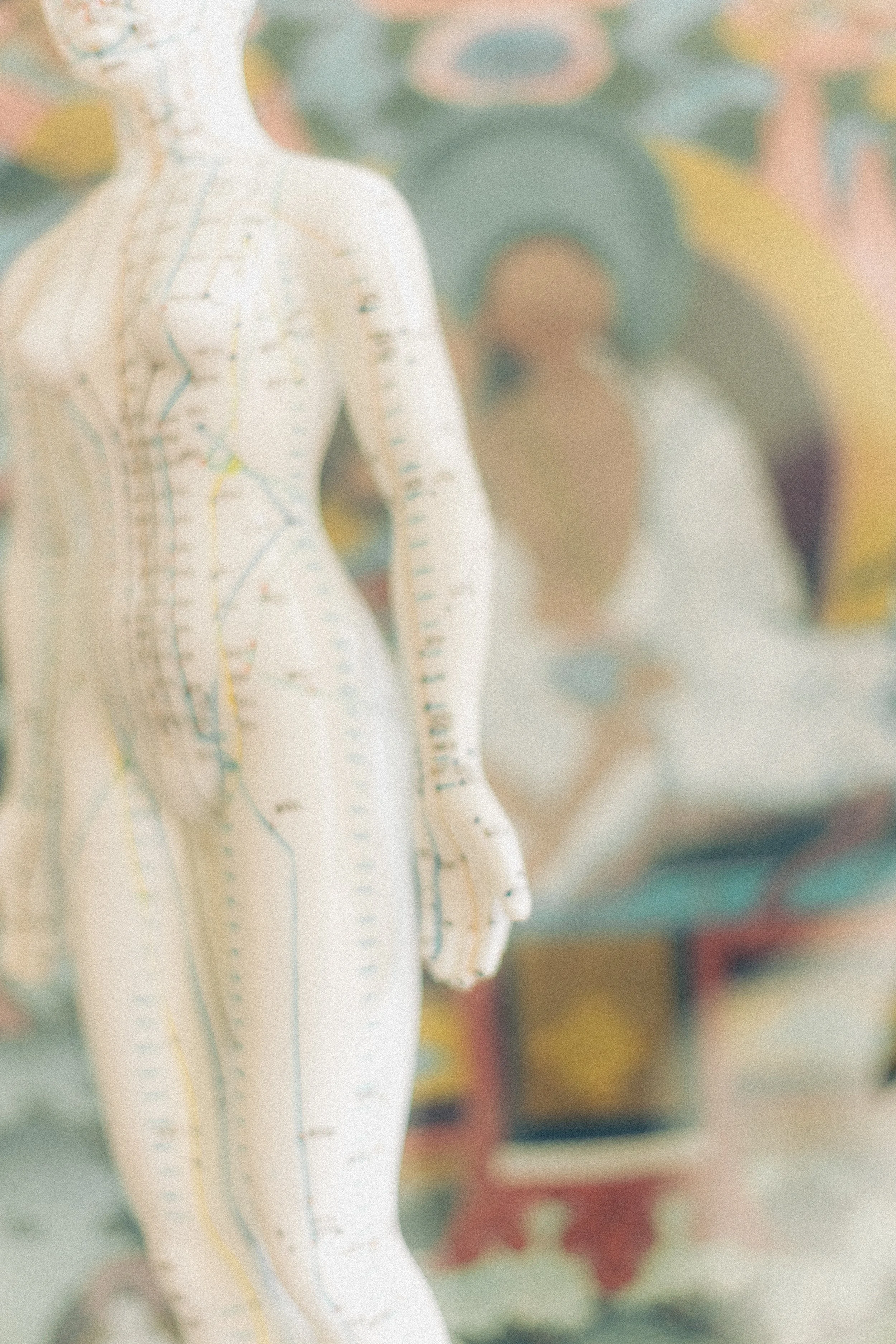 Een model van een menselijke figuur met acupunctuurpunten en meridianen op het lichaam, afgebeeld in een klinische setting met een artistieke achtergrond.