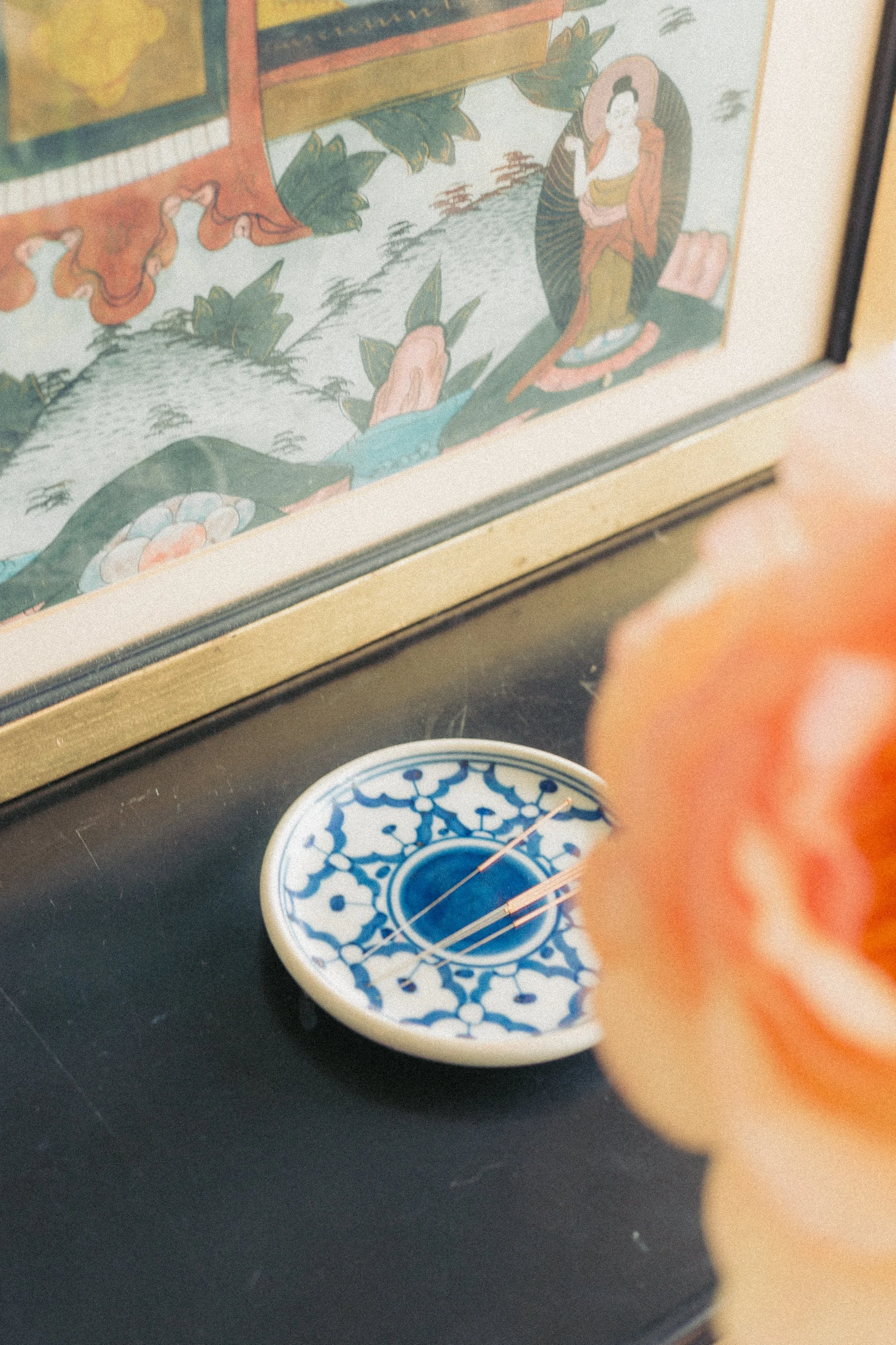 Een boordje met acupunctuur naaldjes, roze bloemen in de voorgrond. Een traditionele Chinese schildering hangt aan de muur.