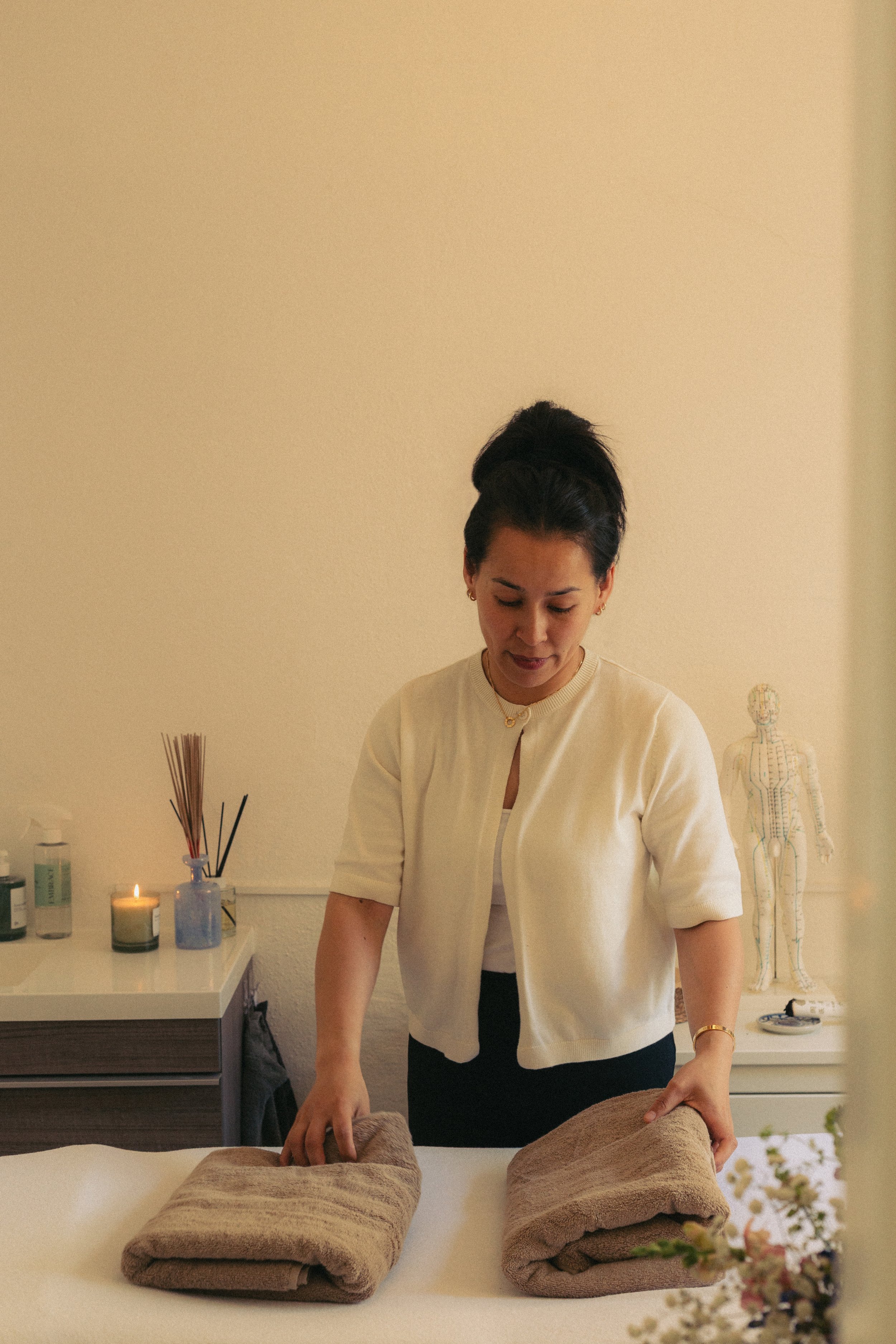 Vrouw die handdoeken oprolt op een massage tafel in een acupunctuur praktijk.