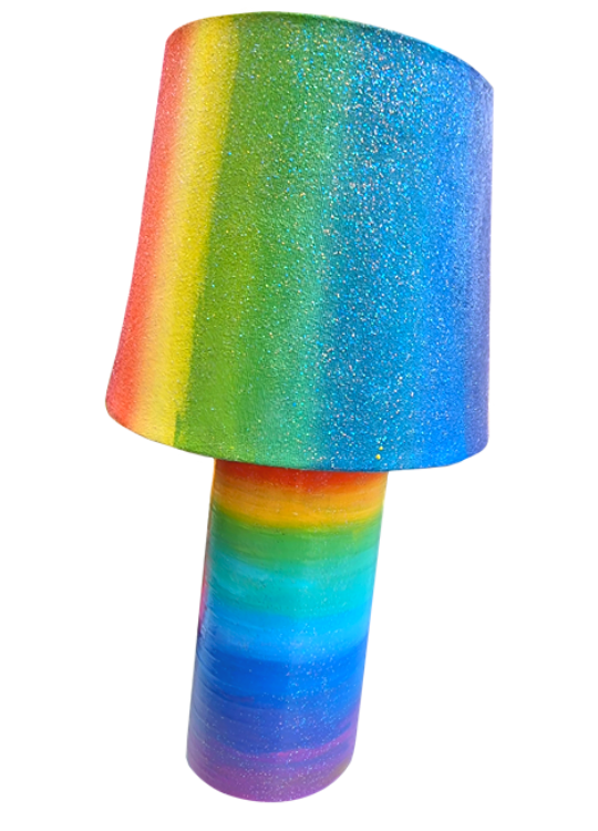 A Colourful rainbow lamp with a rainbow-striped base and a rainbow shade covered in glitter.