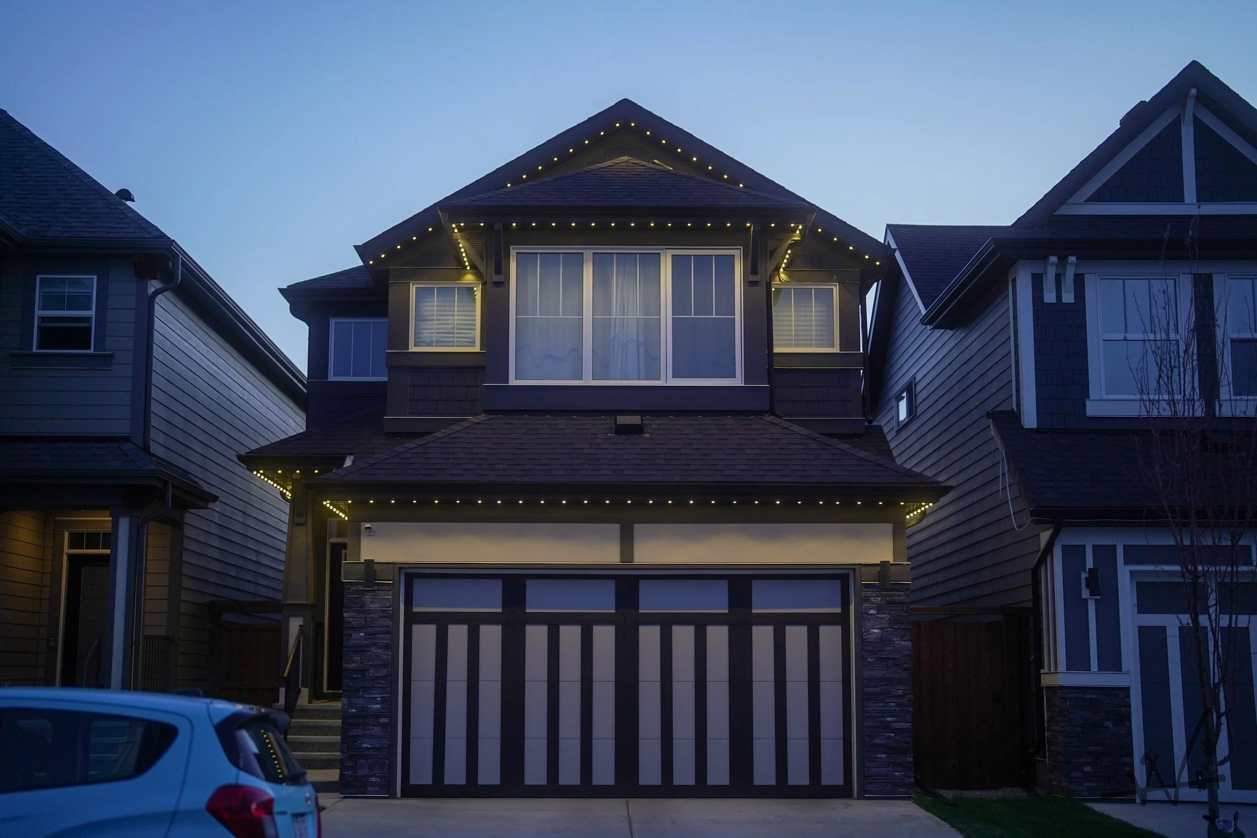 Modern two-story house at dusk with exterior lighting and a striped garage door
