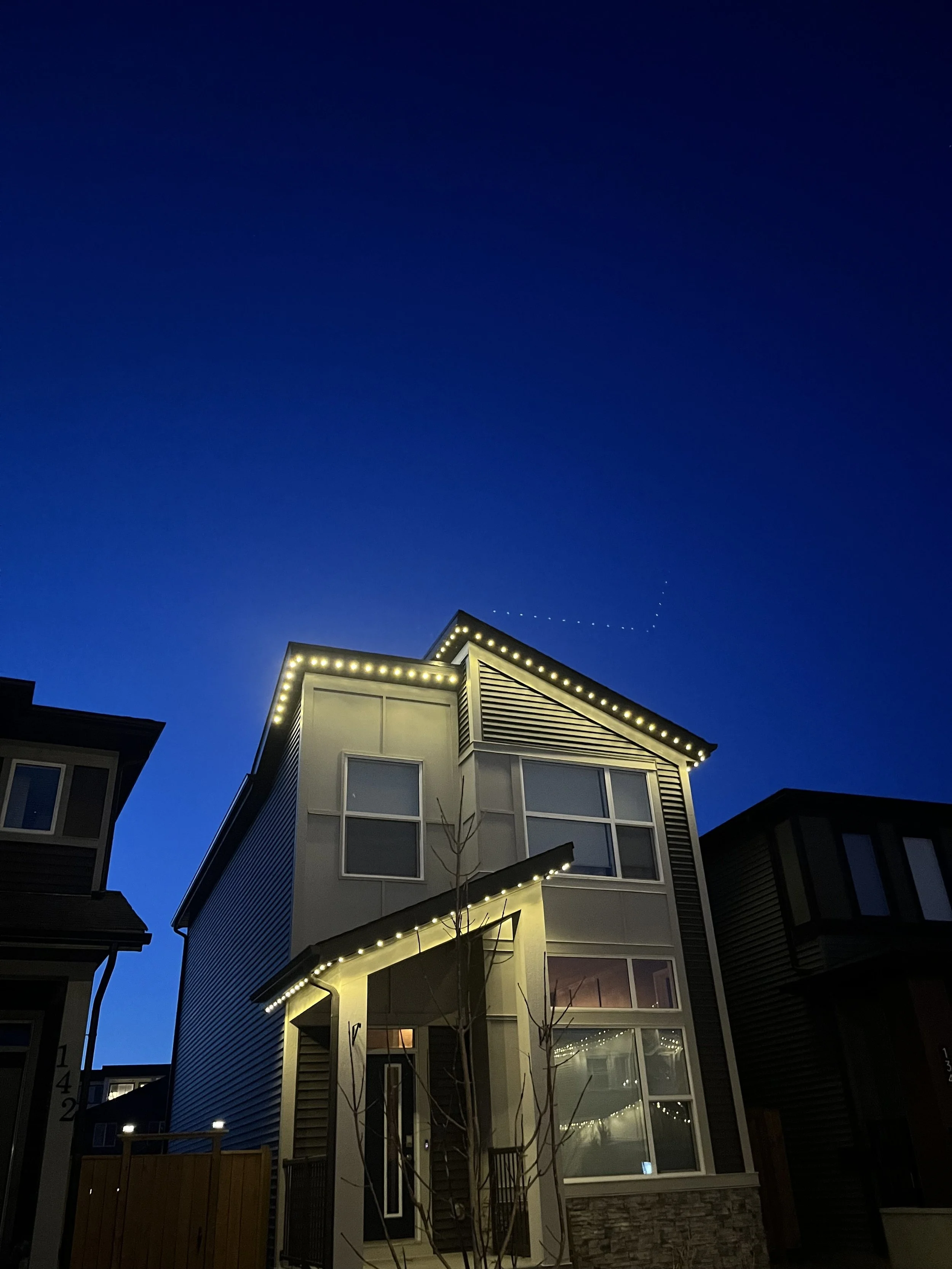 Modern multi-story house at dusk with permanent track lighting outlining the roof and windows
