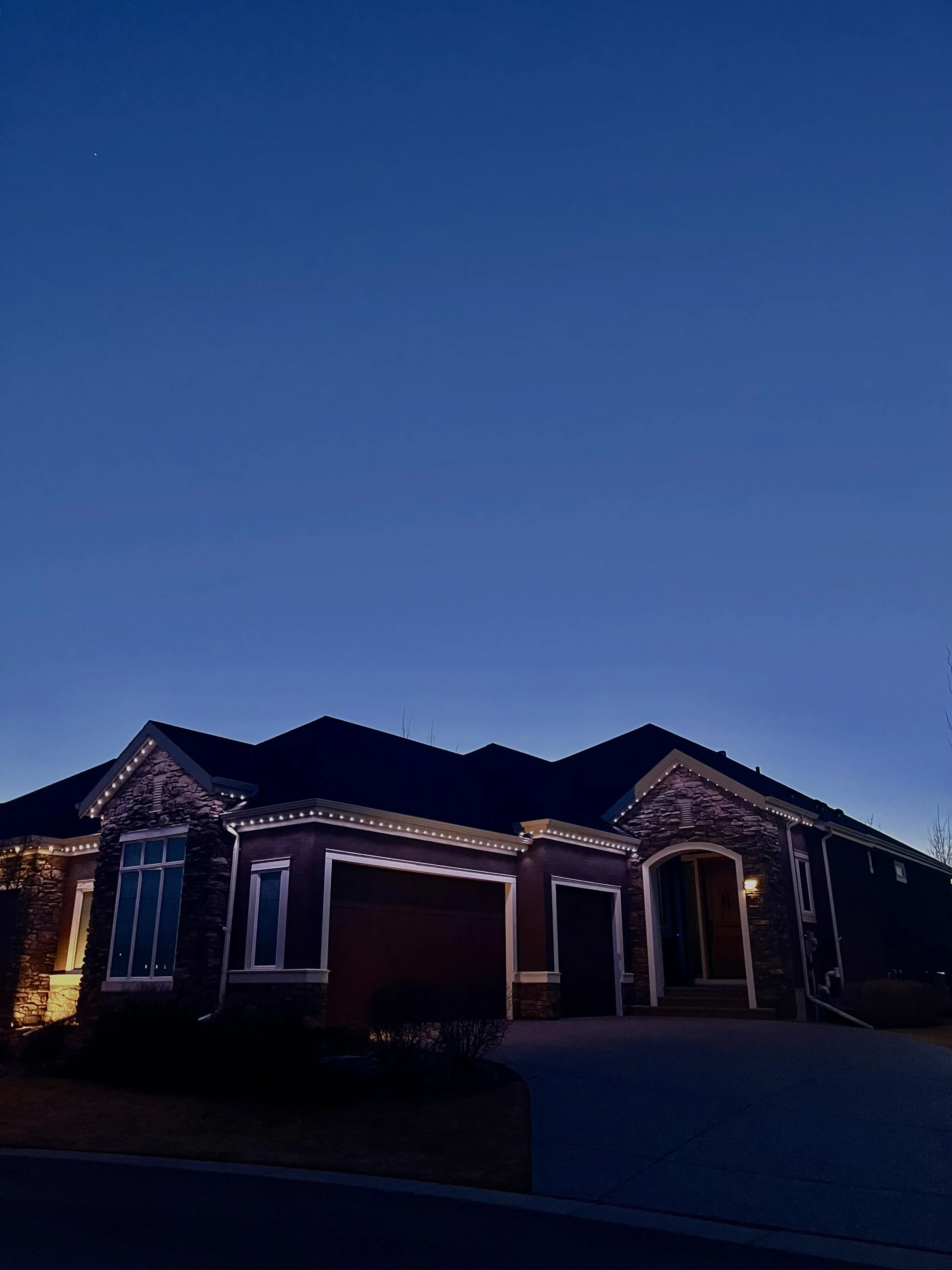 A house at dusk with permanent track lighting along the roofline, dark sky in the background.