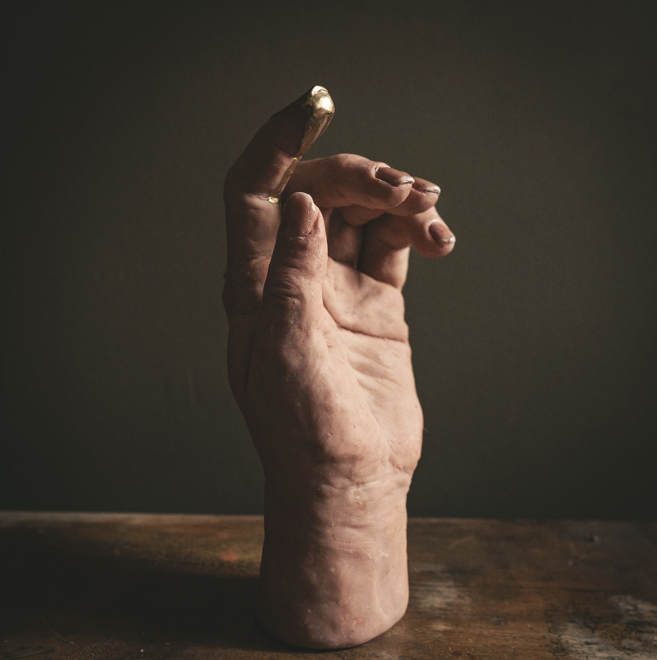 A close-up of a weathered hand with onycholysis and nail polish, raising fingers against a dark background.