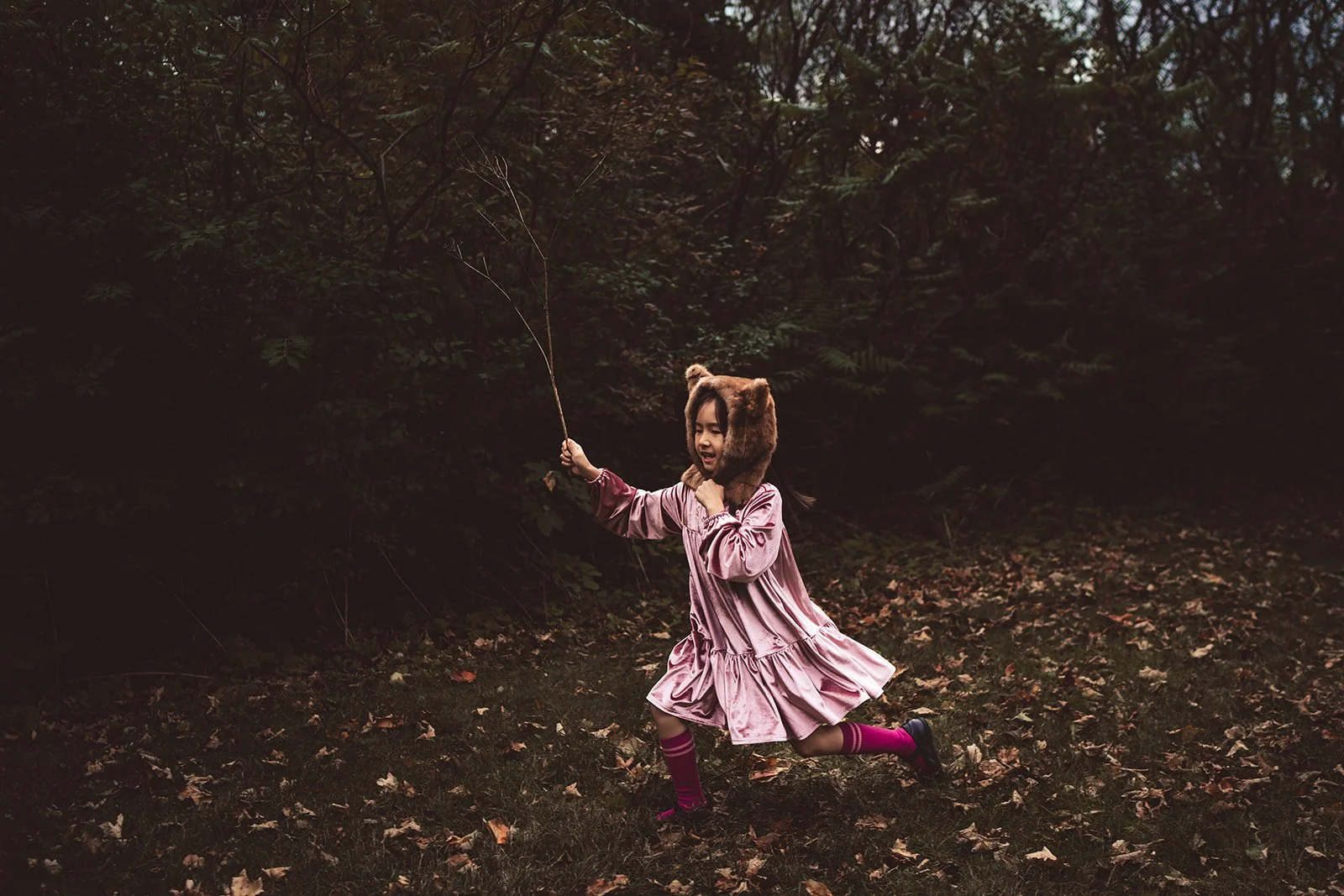 A young girl in a fox hat with ears brandishes a stick while playing an imaginary game