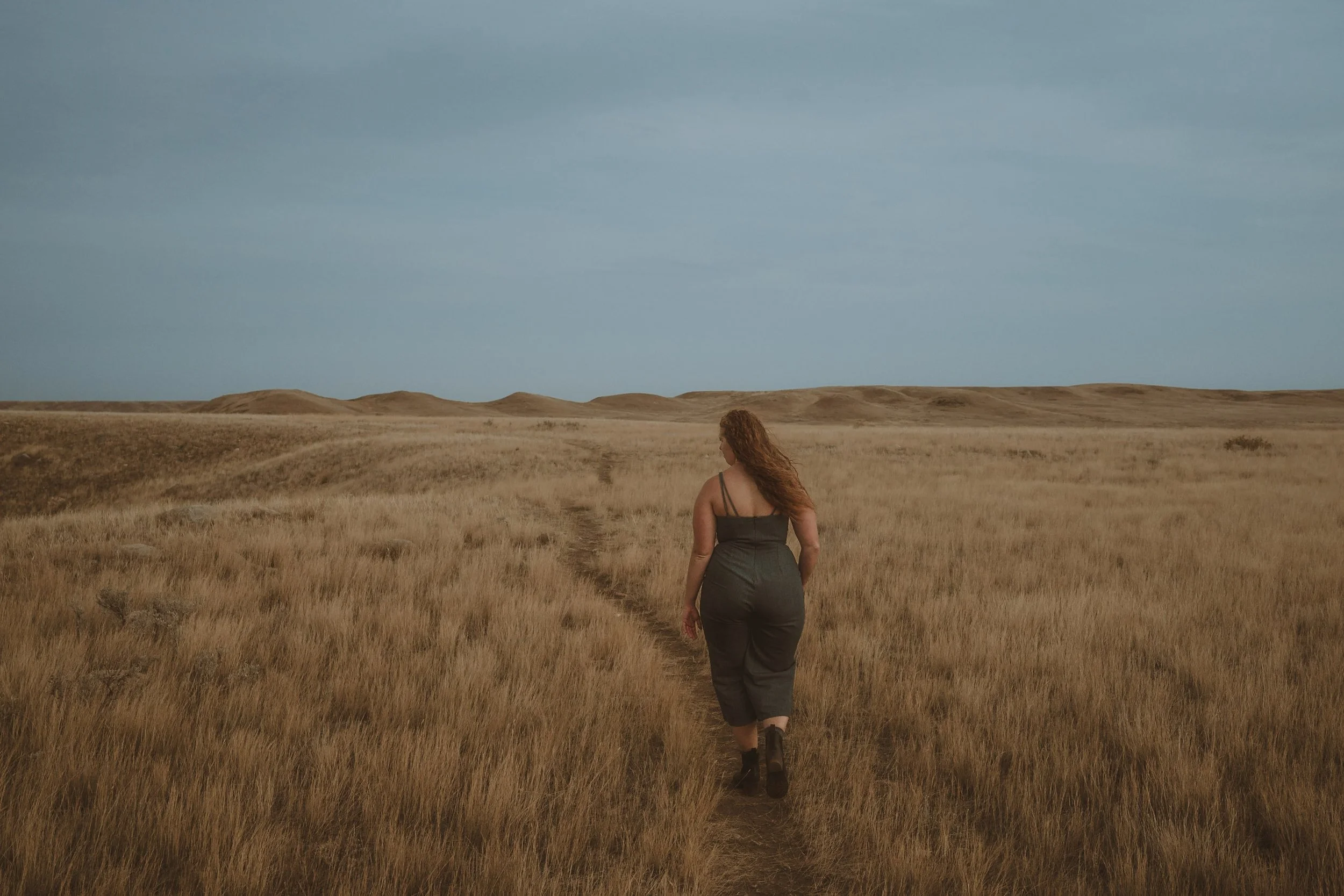 Woman walking through a grassy field under a cloudy sky.