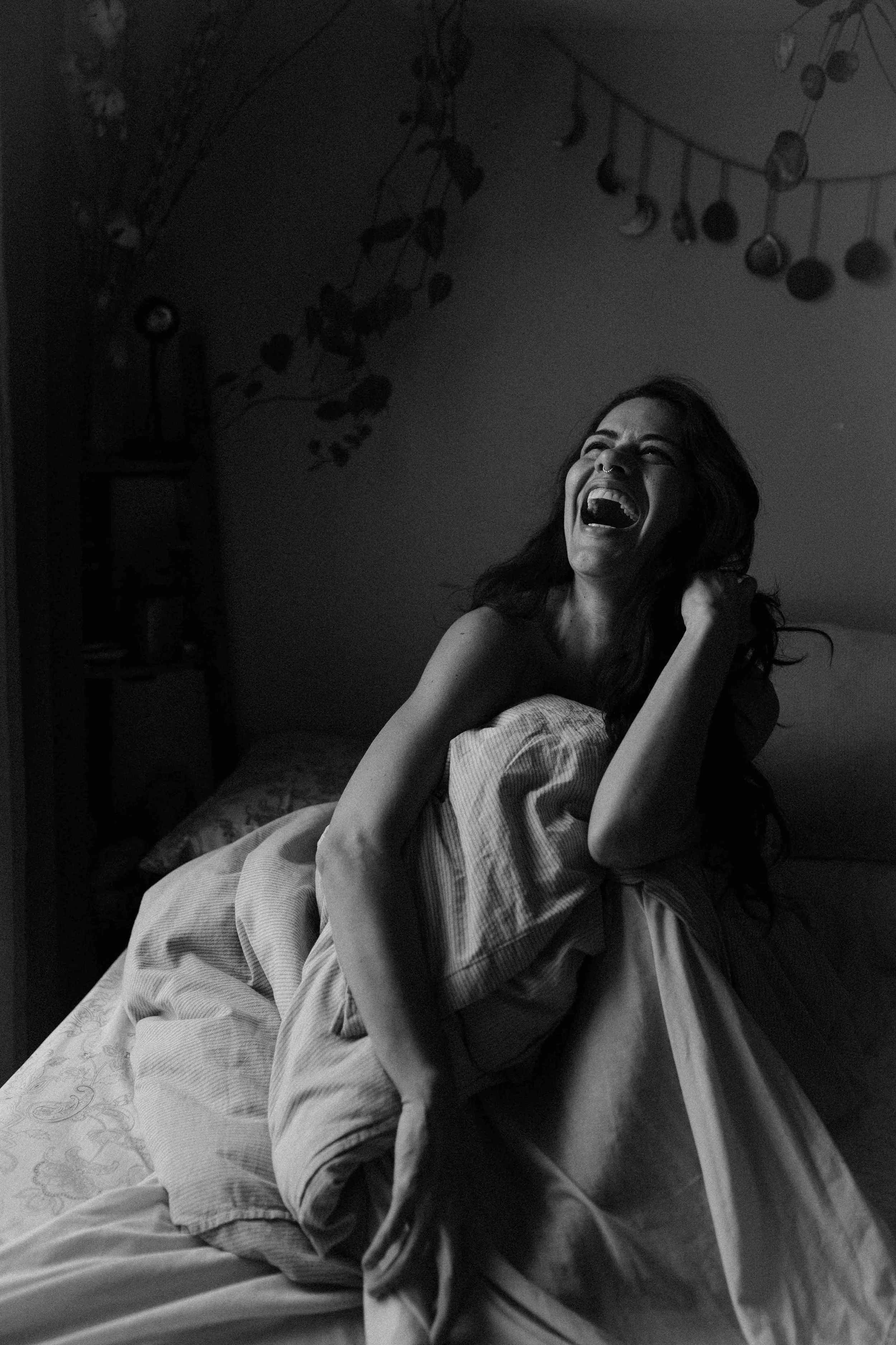 A woman laughing on a bed with a quilt, in a dimly lit room with moon phase decorations hanging from the ceiling.