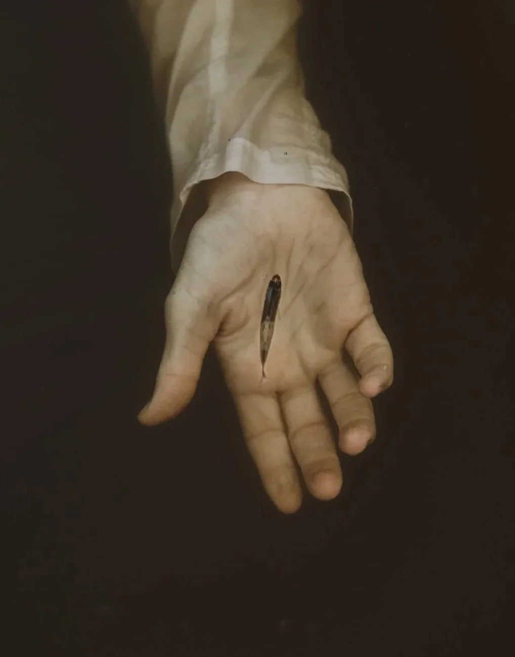 Close-up of a worn, dirty hand with a long scar or wound in the middle of the palm, against a dark background.