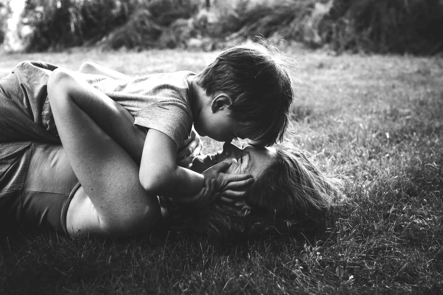 A woman lying on a bed of ferns with her legs extended and one arm behind her head, wearing a beige dress with embroidery.