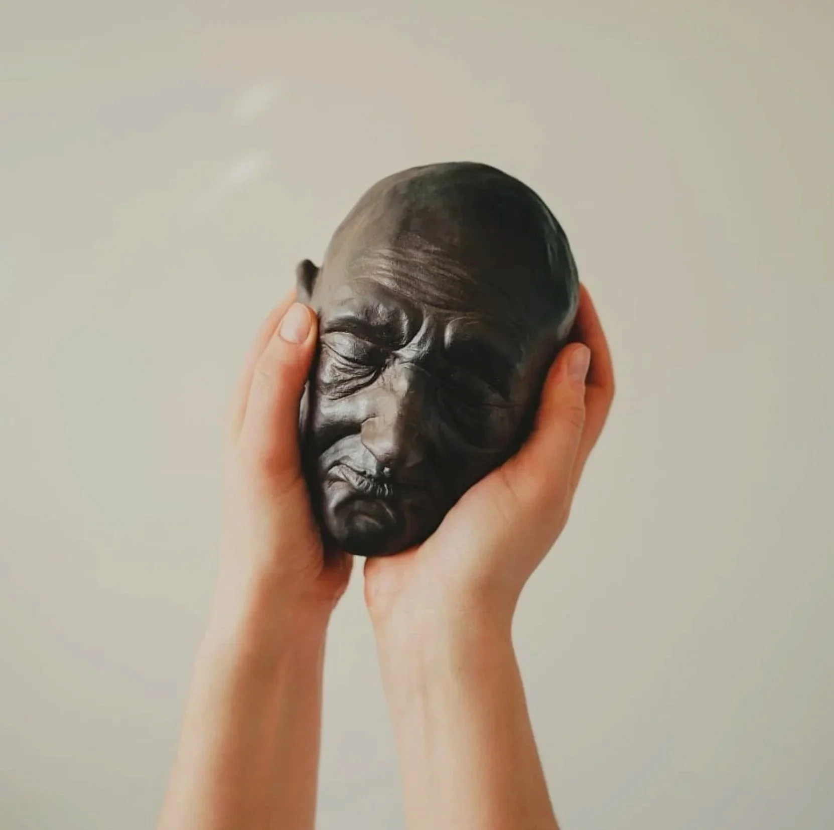 Hands holding a black sculpture of a person's head with detailed facial features and closed eyes.