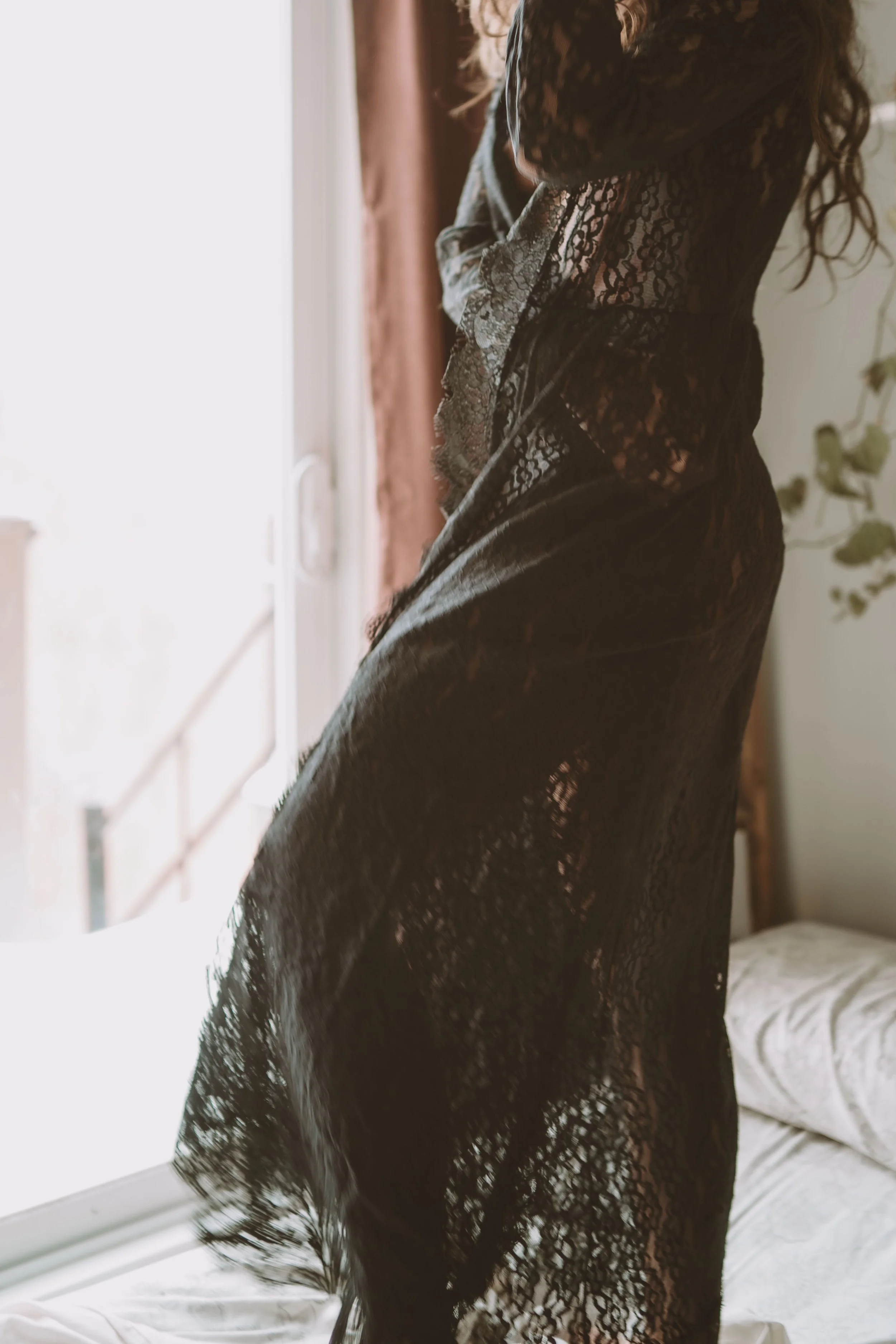 Person in black lace dress standing by a window with light streaming in.