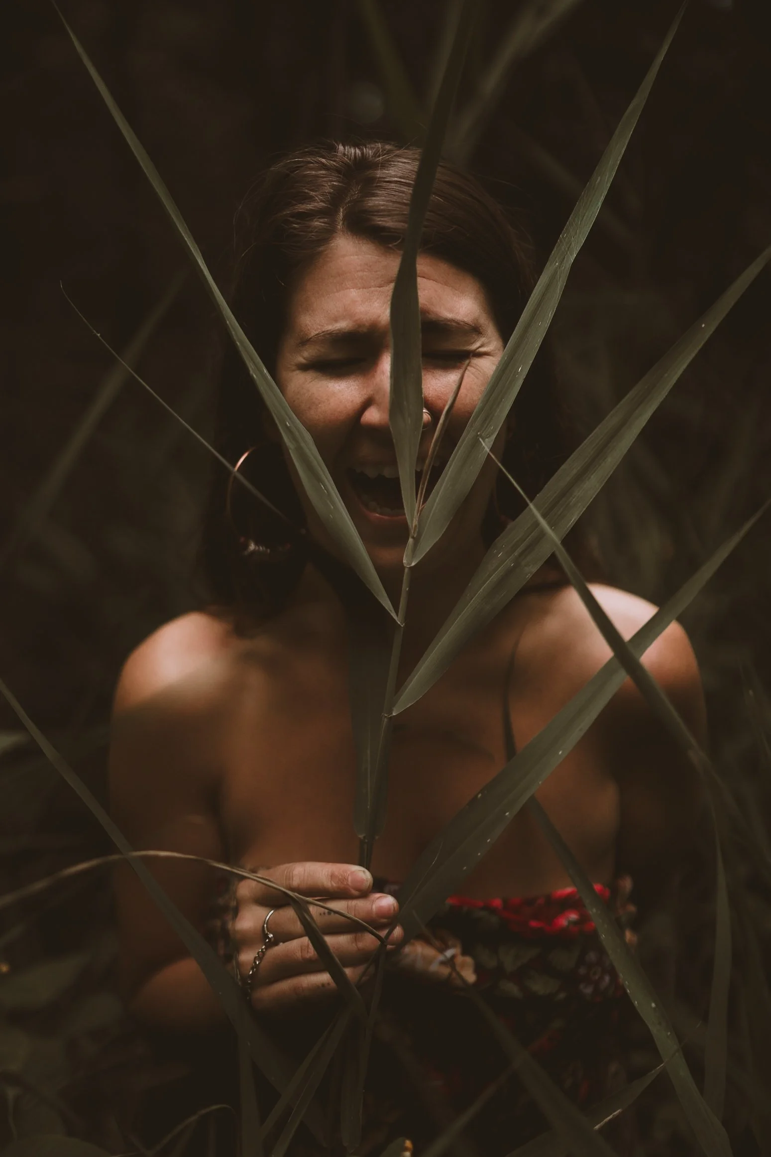 A woman holds up a fern leaf in the forest while laughing joyfully