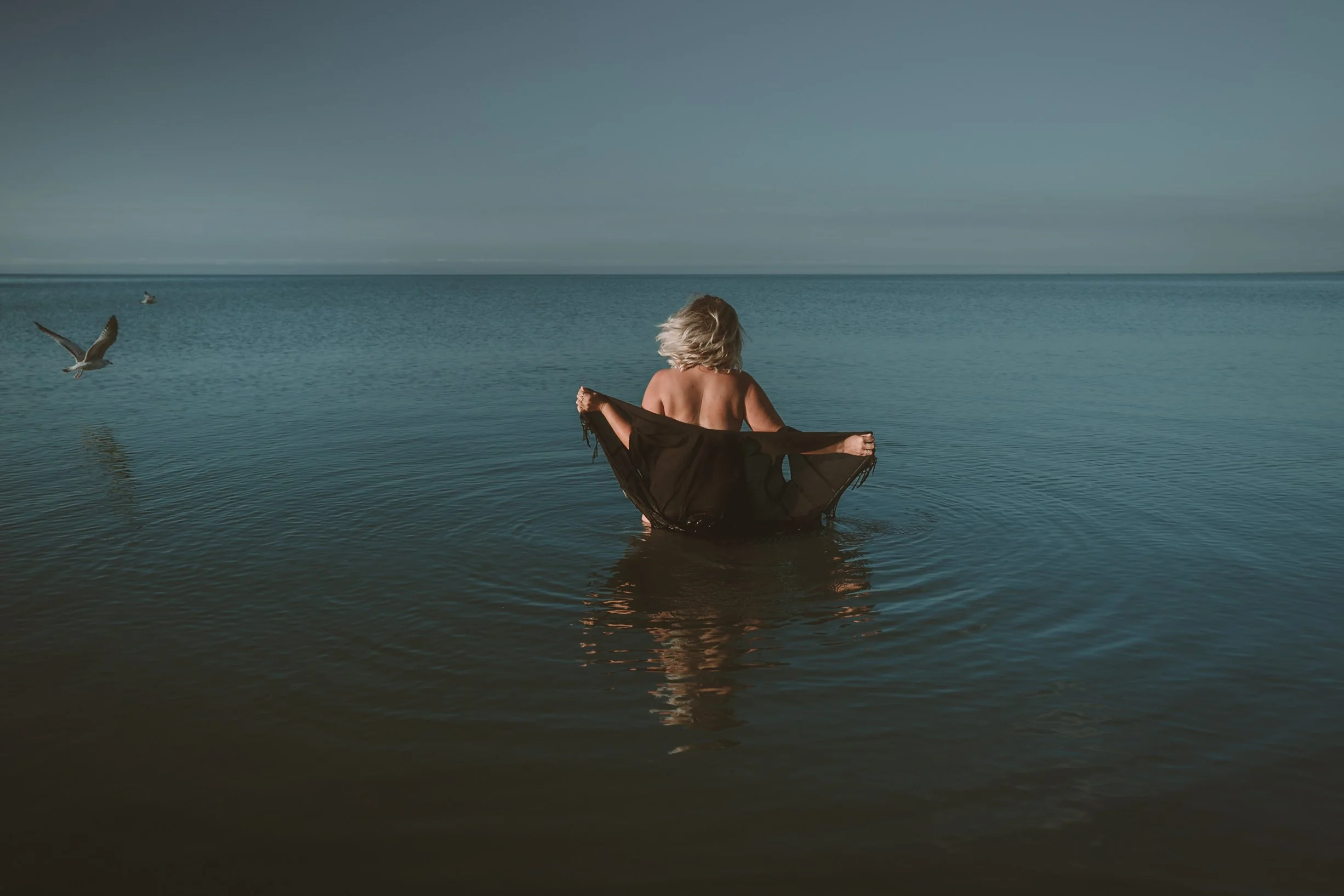 A woman runs into azure water as birs fly by