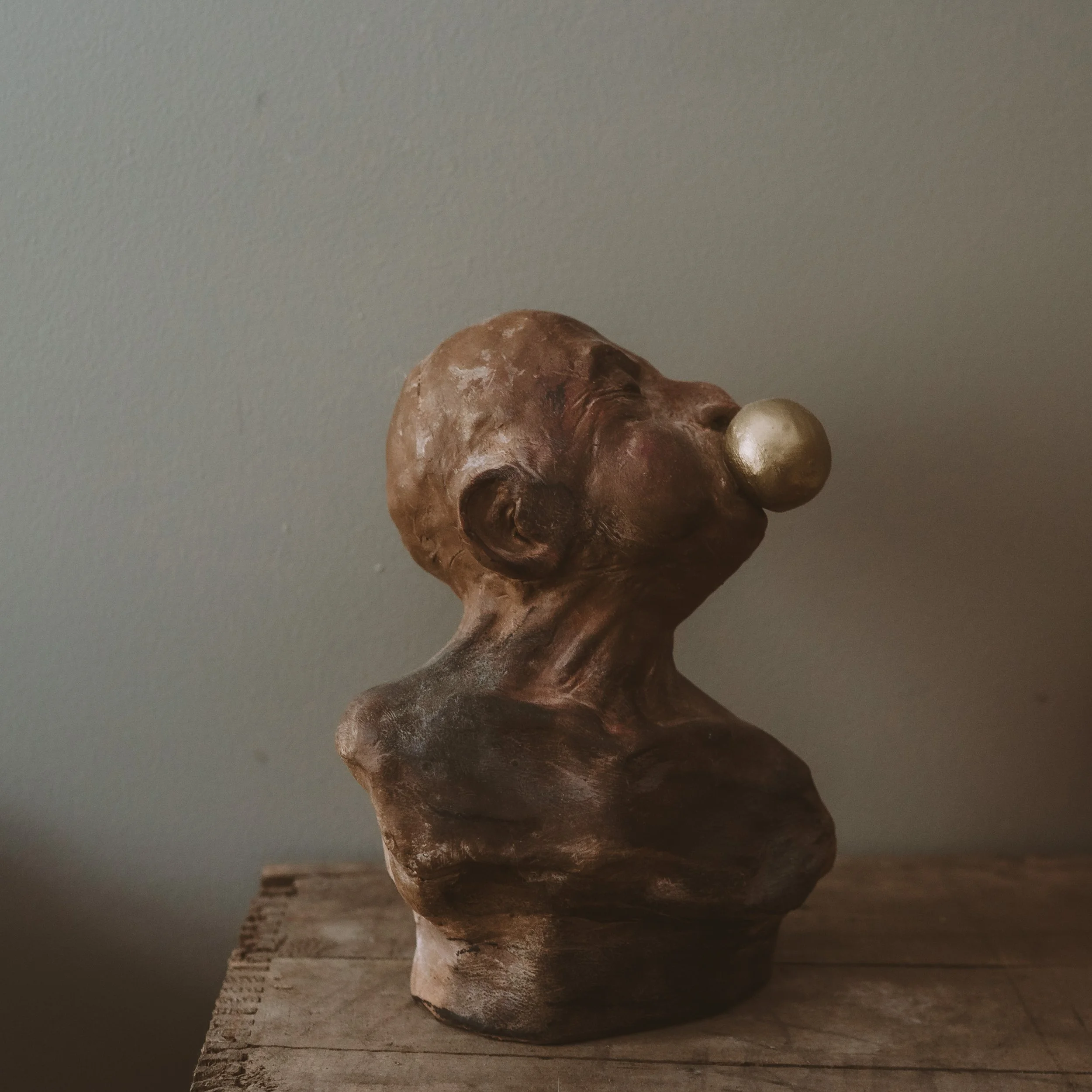 Close-up of a decorative wooden sculpture with a carved face, placed on a wooden surface against a neutral gray wall.