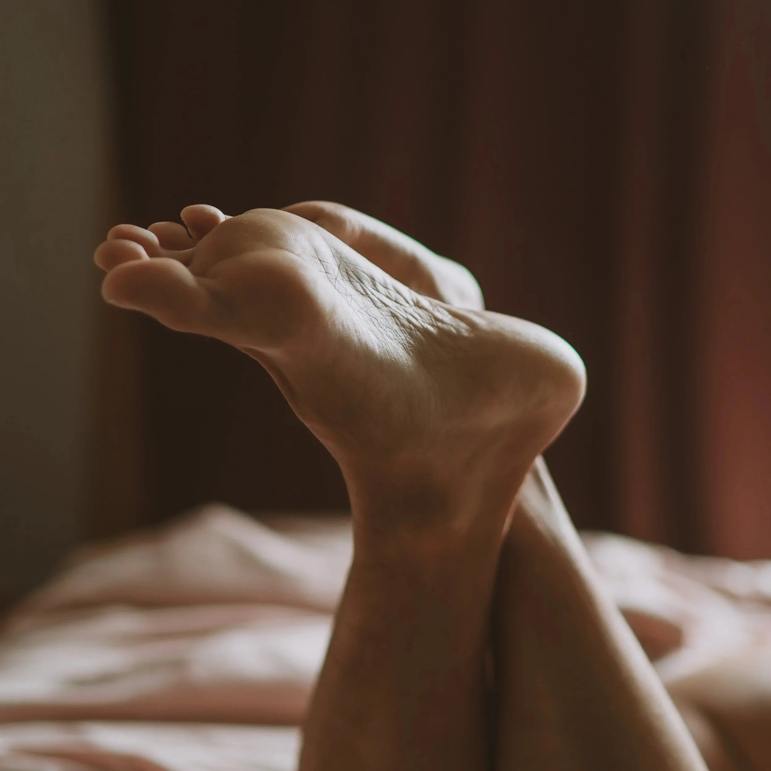 Close-up of a person's hand and foot with natural light, showing wrinkles and skin texture, with a blurred background.
