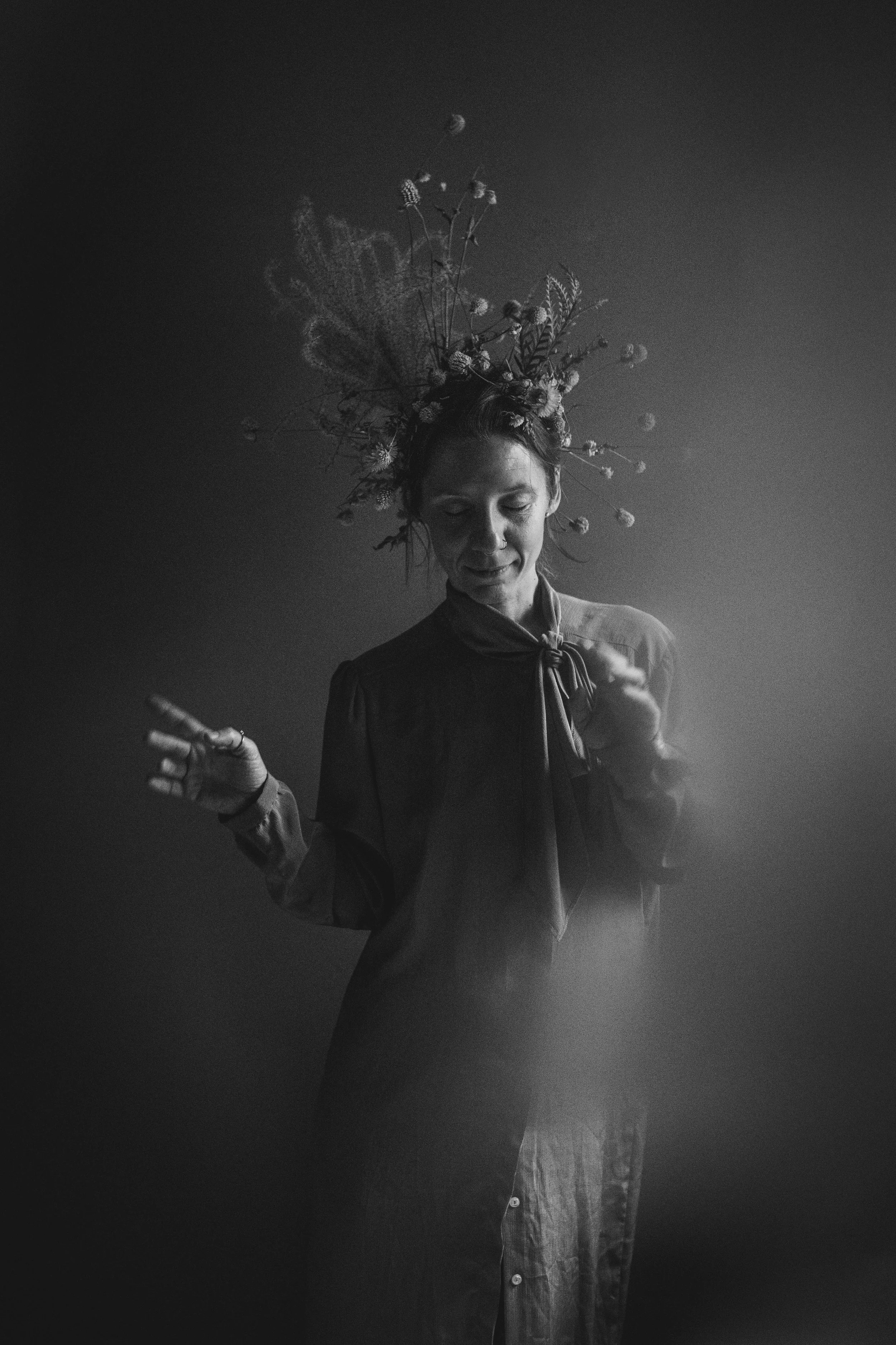 Black and white portrait of a woman with her eyes closed, wearing a long dress and a ribbon around her neck, with an elaborate floral headdress and a moon in the background.