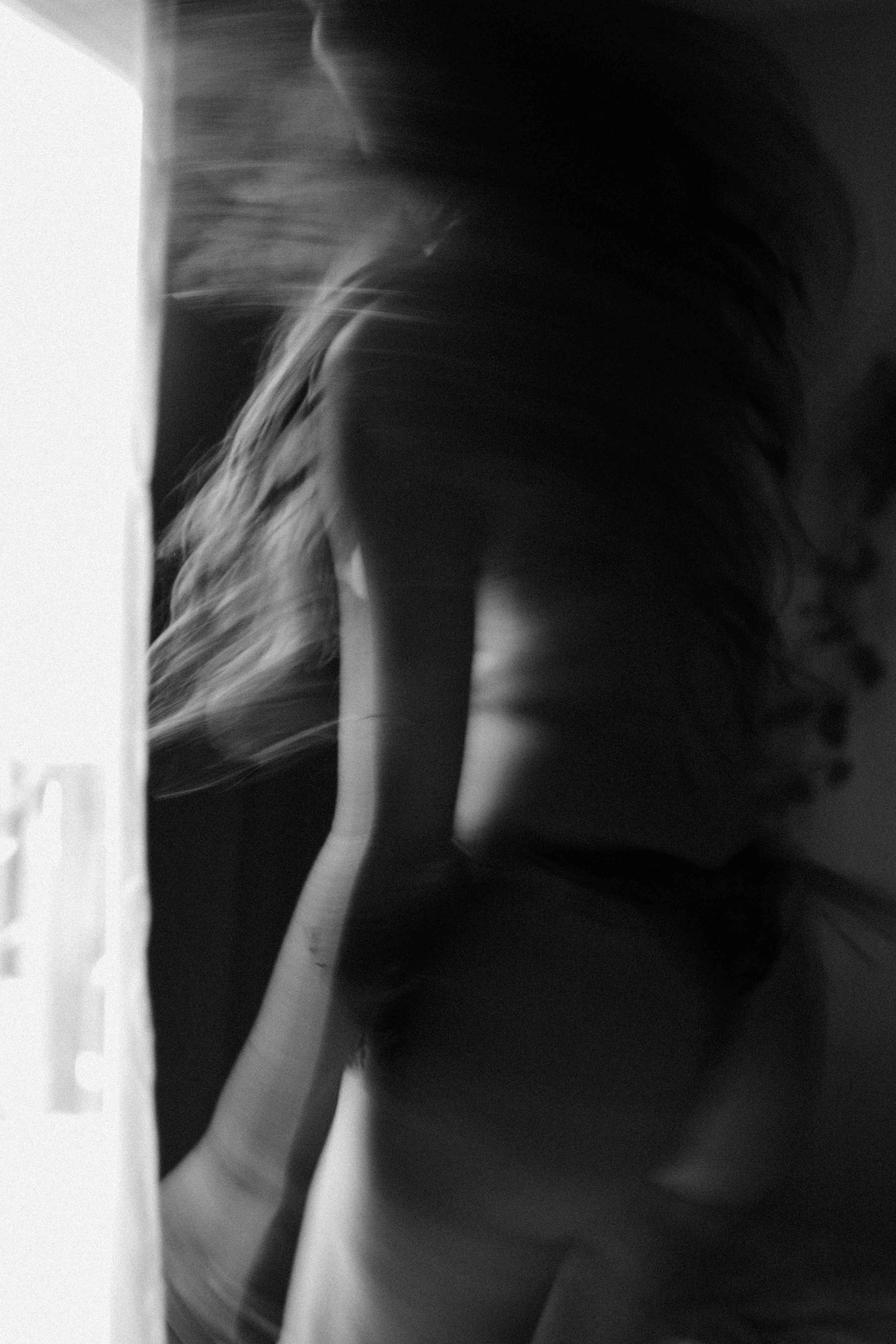 A partially obscured figure is seen from behind, with long hair and an arm raised. The scene appears to be indoors with lighting creating shadows.