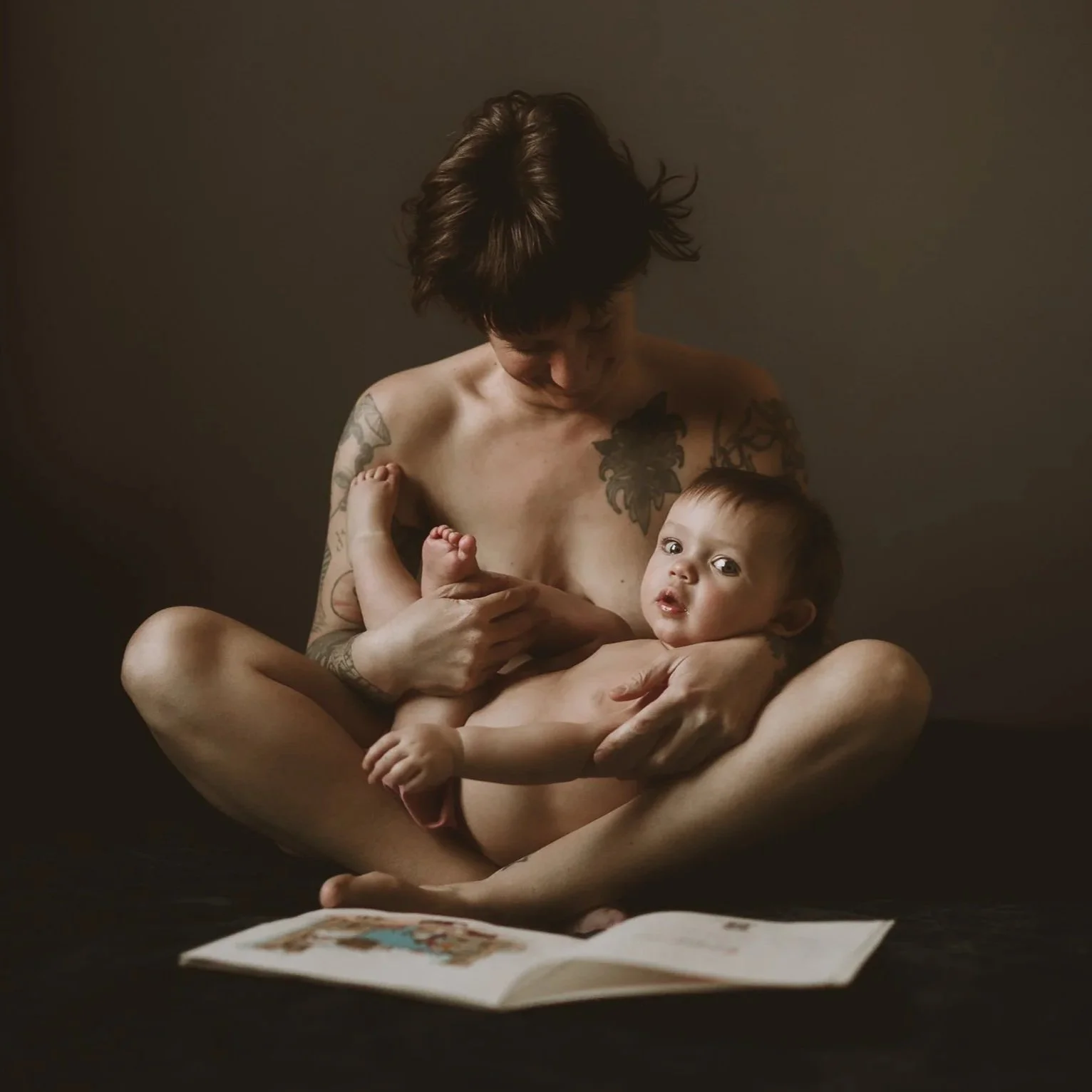 A person with tattoos holding a baby in a dimly lit setting.