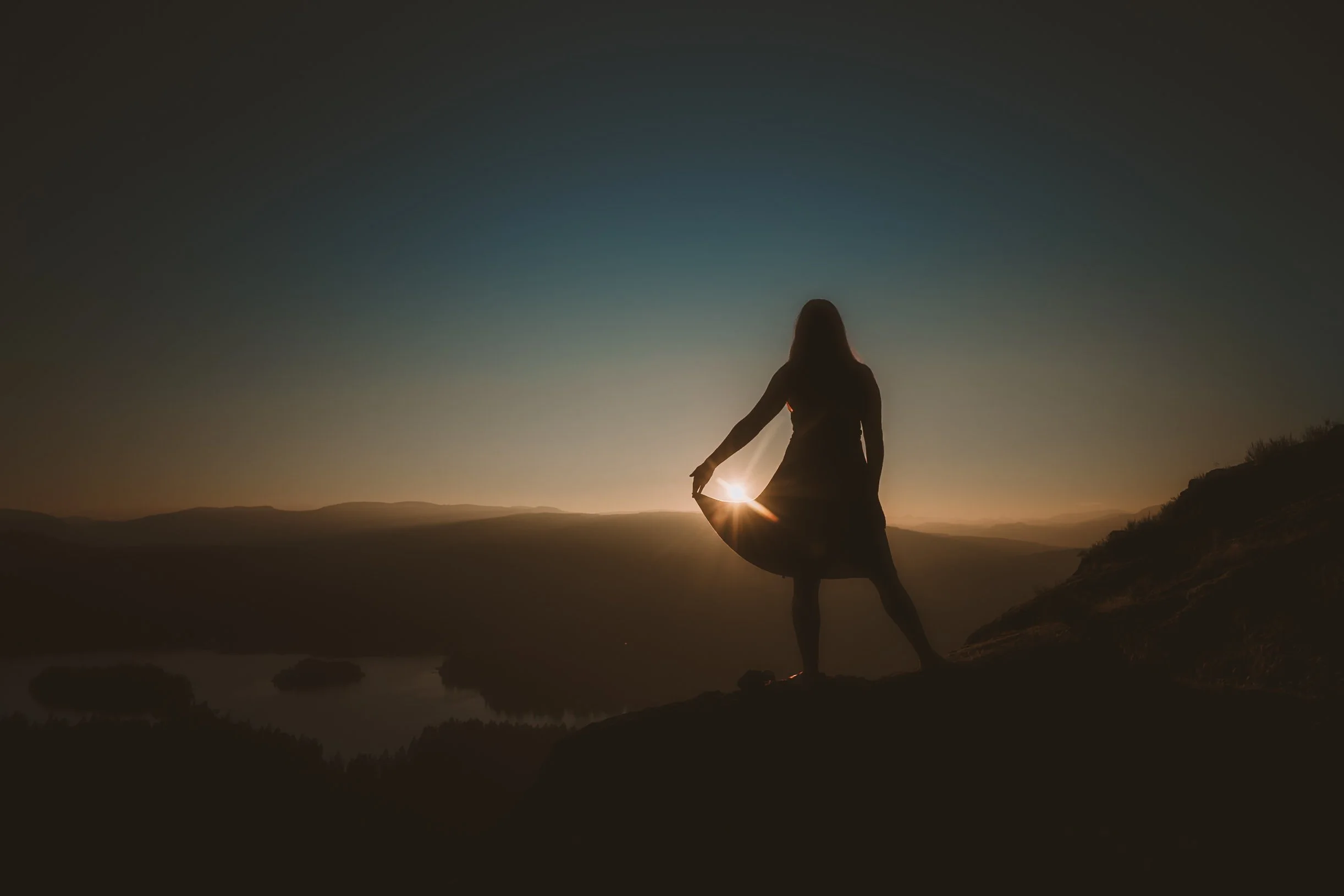 A person practicing yoga outdoors at sunset or sunrise on a mountain or hilltop, silhouetted against a colorful sky.