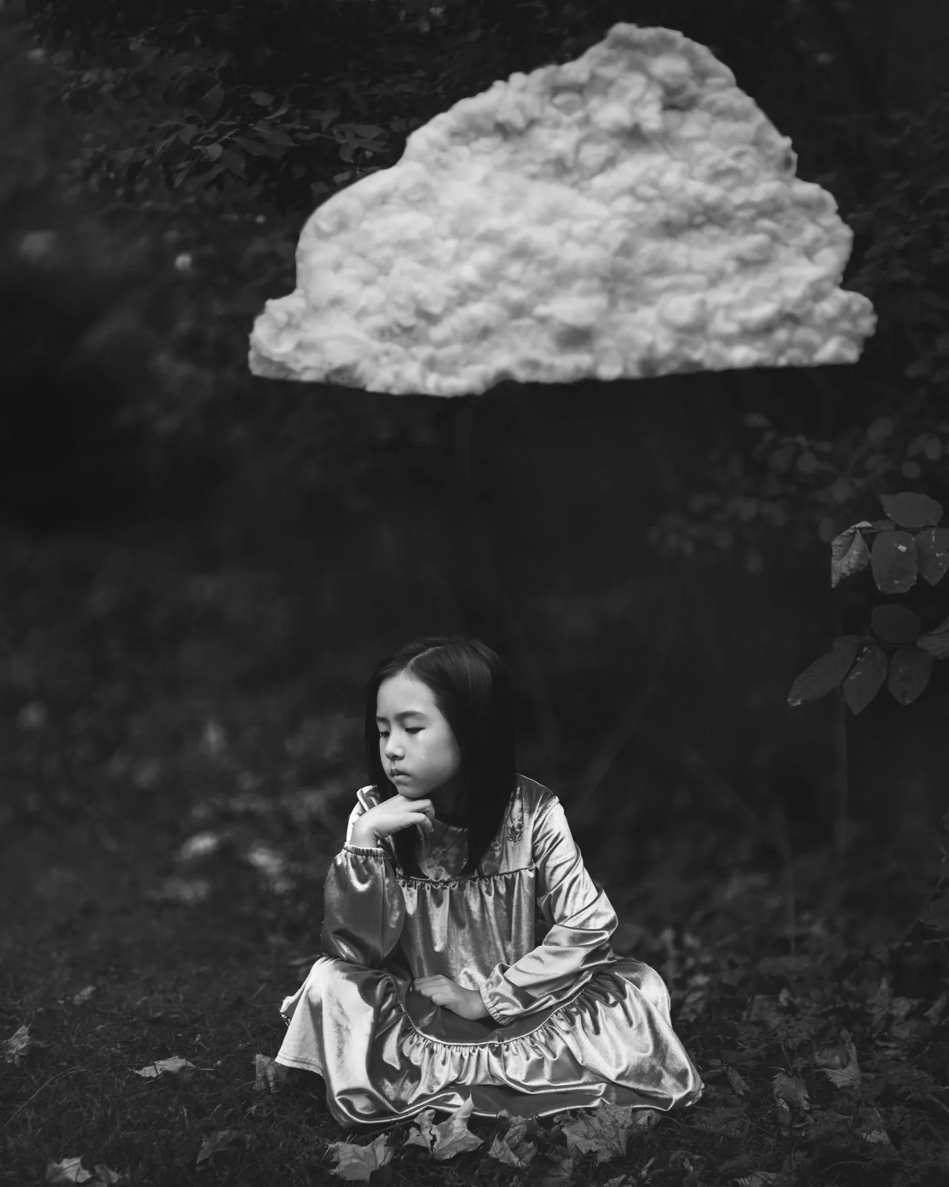 A young girl in a shiny dress sitting on the ground outdoors, looking thoughtful, with a large cloud floating above her.