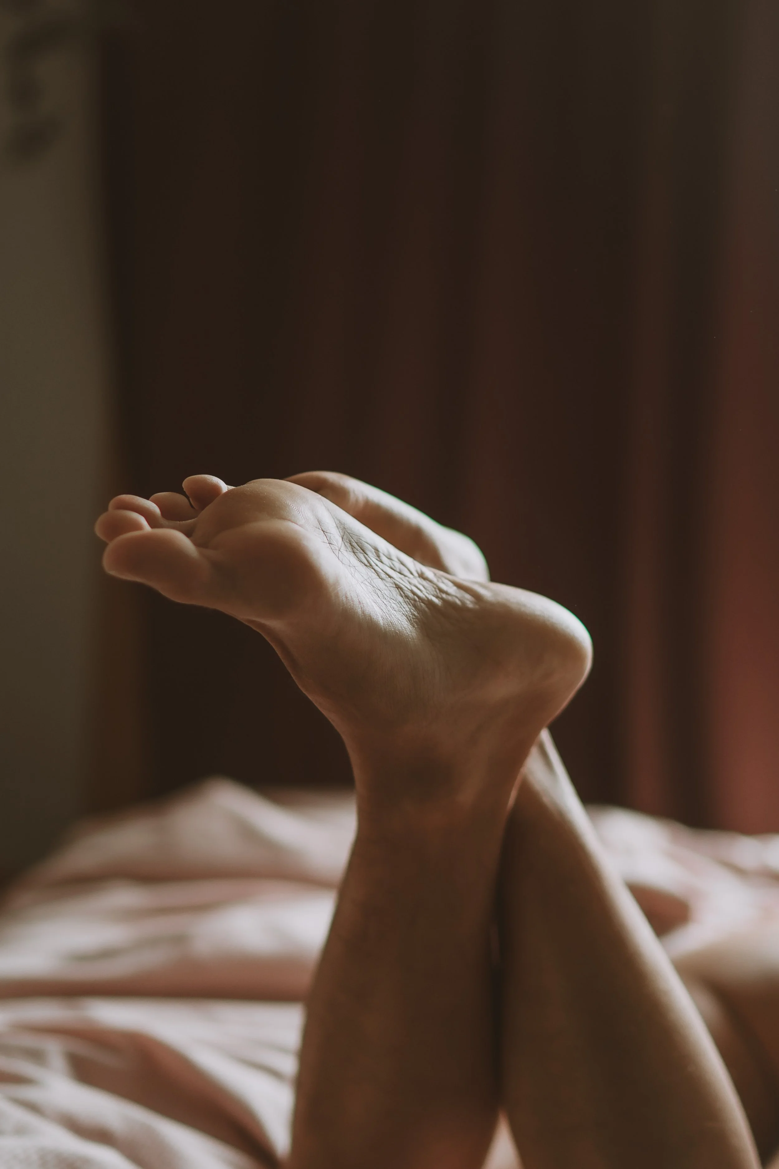 Close-up of a person's hand resting on their face, with fingers gently touching the cheek, soft lighting creating shadows and highlighting skin texture, against a blurred dark background.