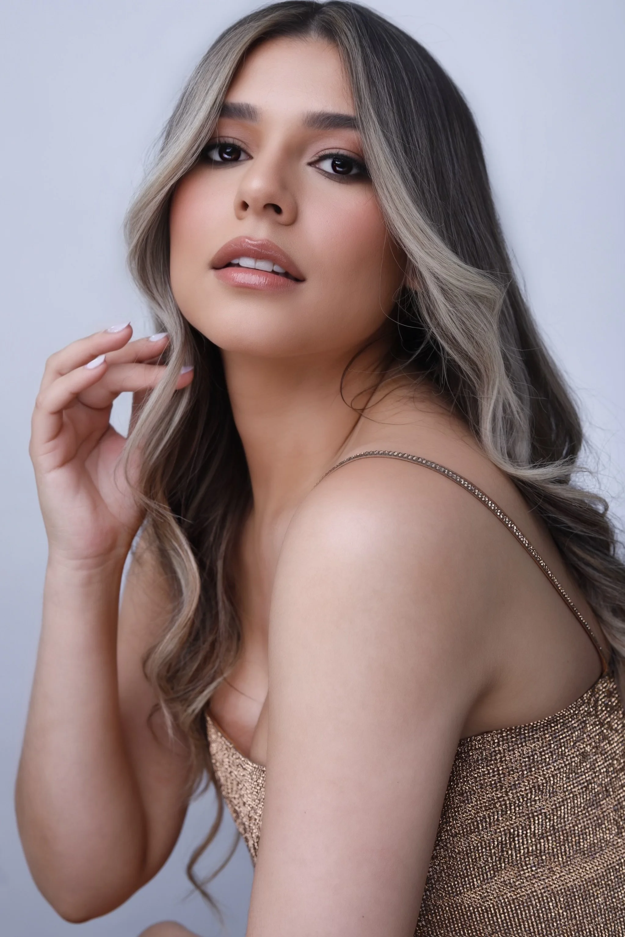 A woman with long, wavy hair and light makeup wearing a sparkly, sleeveless top, looking at the camera with a relaxed expression.