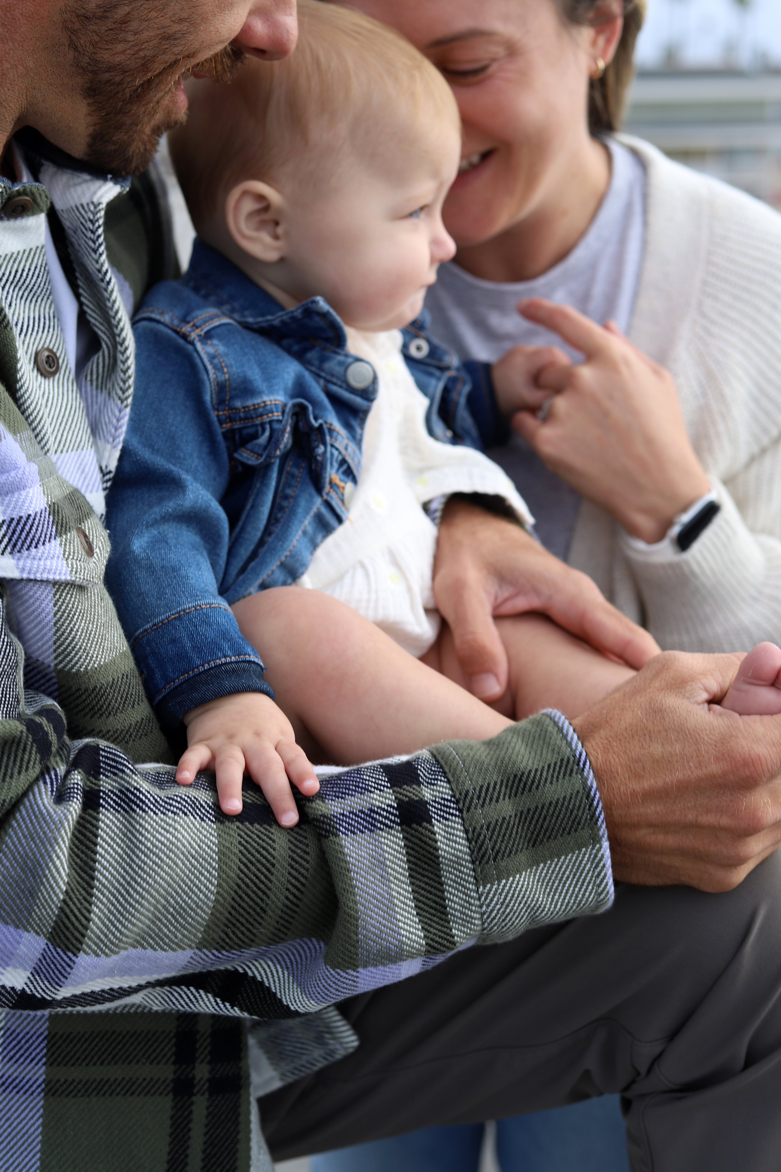 Close-up of a family moment, with a man and woman holding a young child, all smiling and touching foreheads, outside.