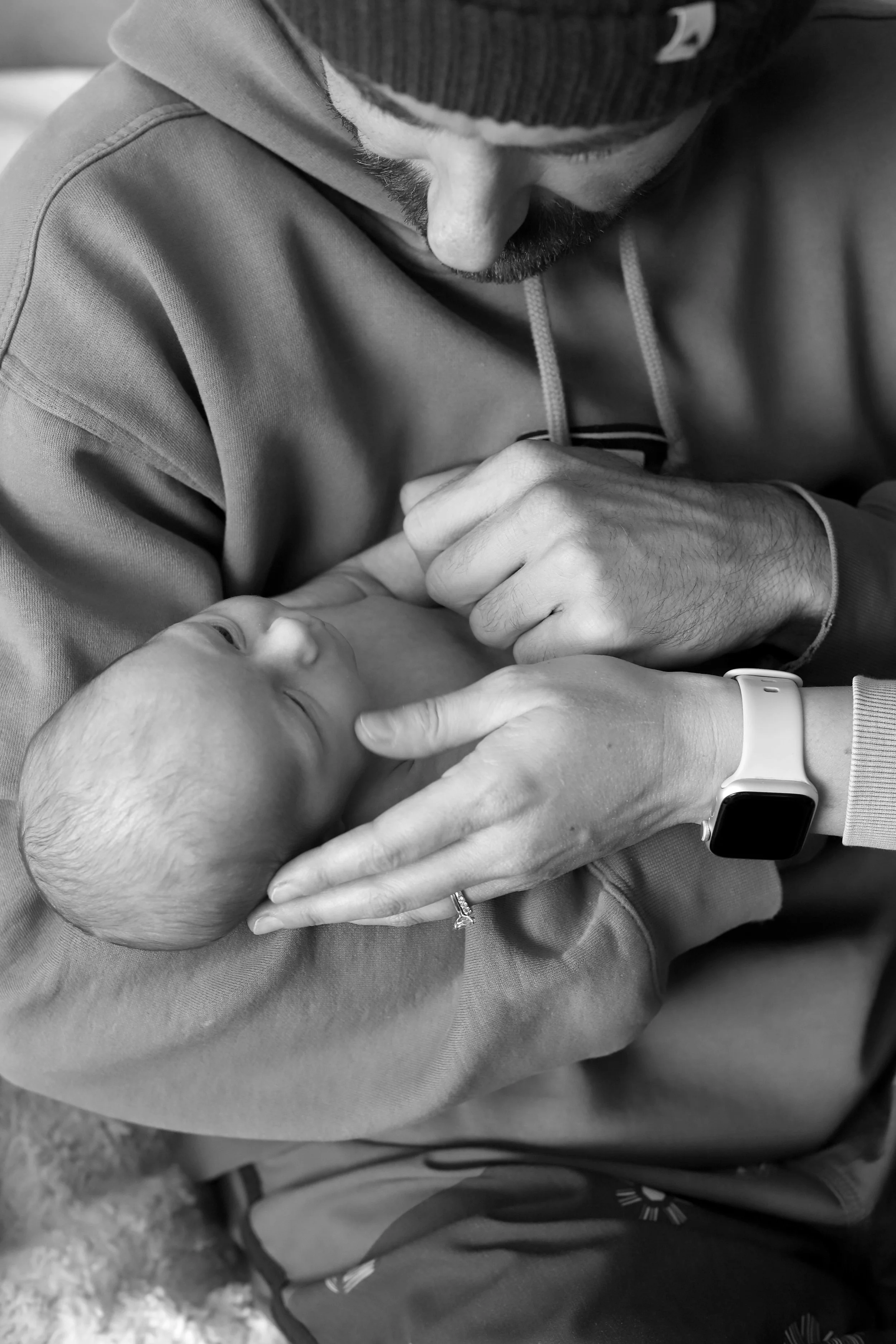 A father is gently holding his newborn baby, appearing to gaze at the baby, in a close-up black-and-white photograph.
