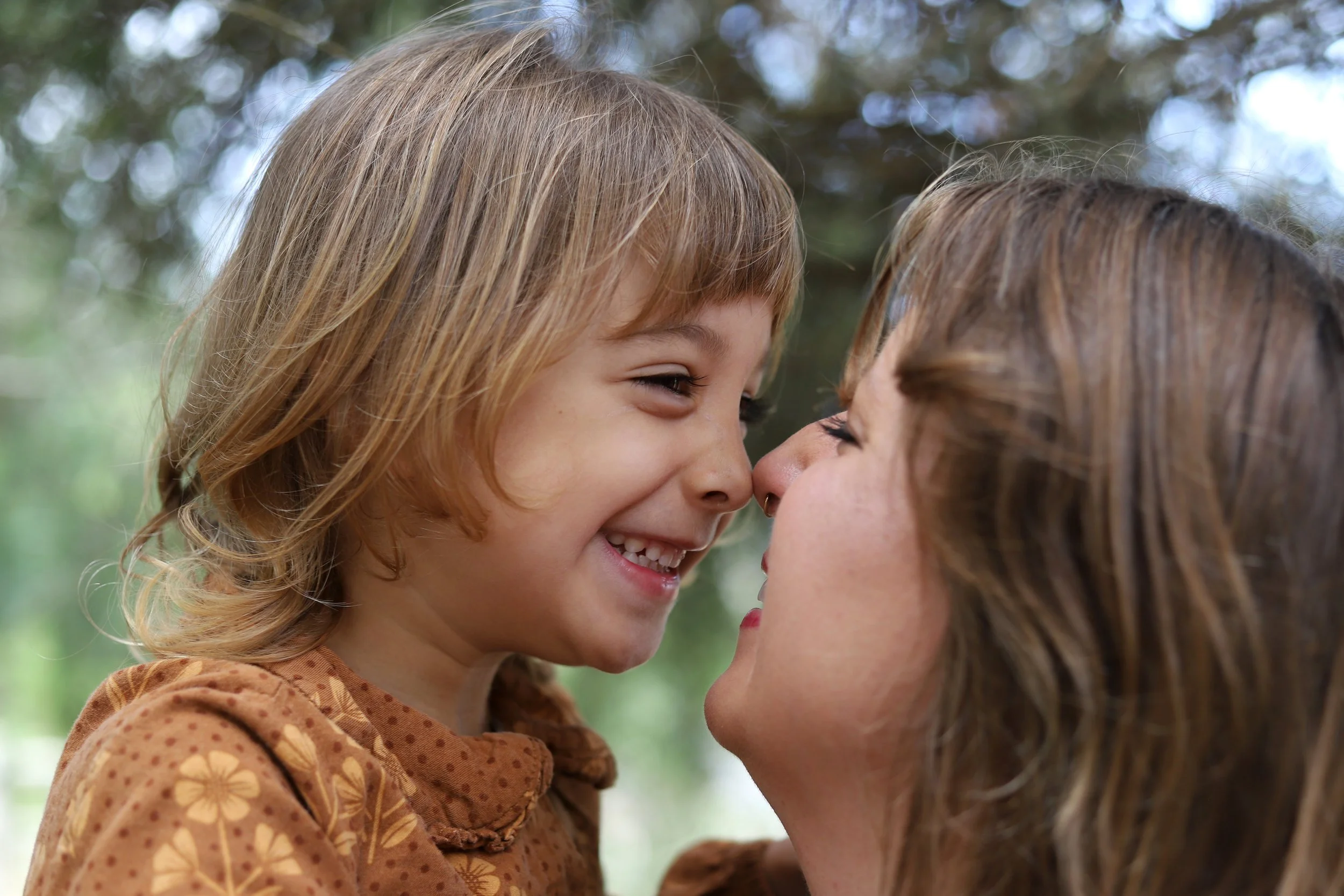 A woman and a young girl are close together, about to touch noses, smiling with joy.