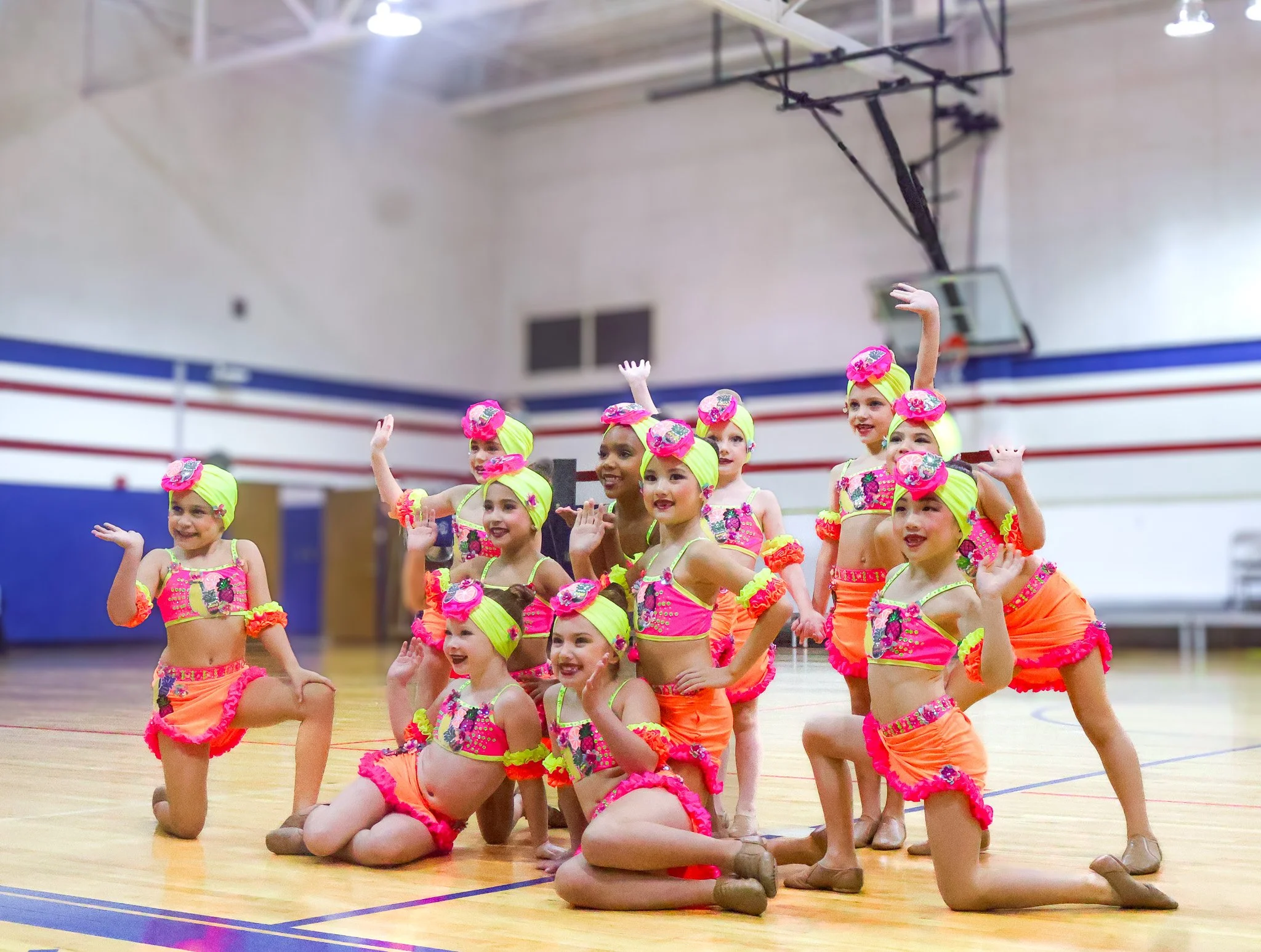 A group of young girls in colorful costumes performing a dance routine in a gymnasium at WDC Dance Competition. The central Texas premier dance competition.
