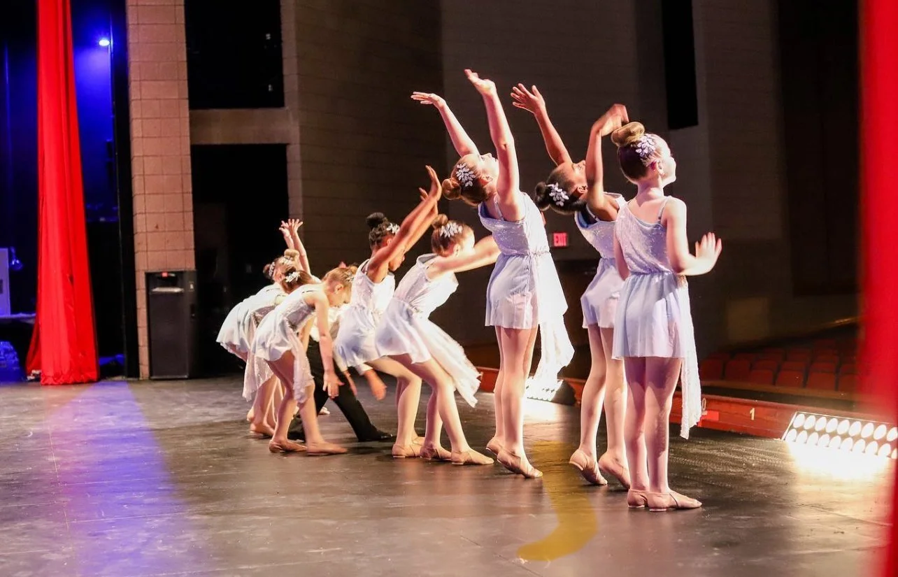 A group of young girls dressed in white costumes taking a bow on stage after a dance performance at WDC Dance Competition in Leander, TX. The premier Central Texas dance competition and contest.