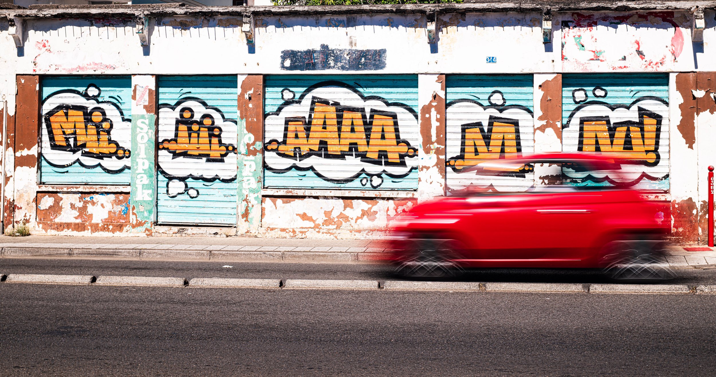 Scène urbaine colorée avec une voiture rouge en mouvement devant un mur couvert de graffitis — Photographe lifestyle à La Réunion