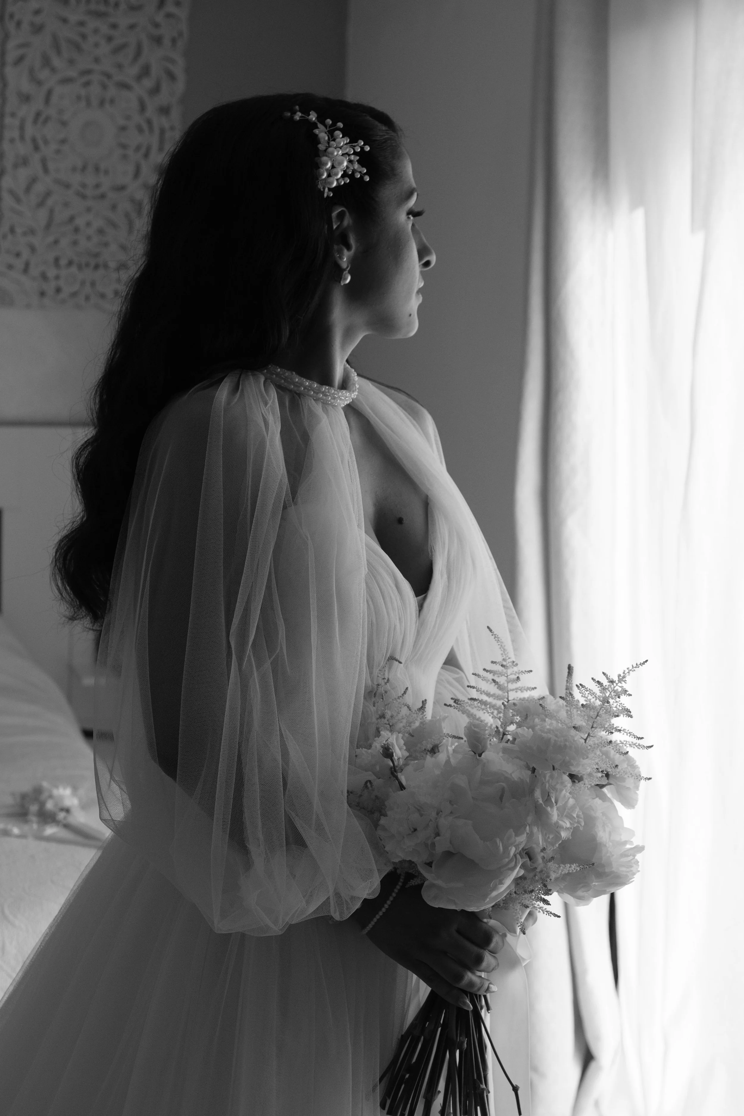 Une femme en robe de mariée tenant un bouquet de fleurs, regardant par la fenêtre. - Photographe mariage à La Réunion