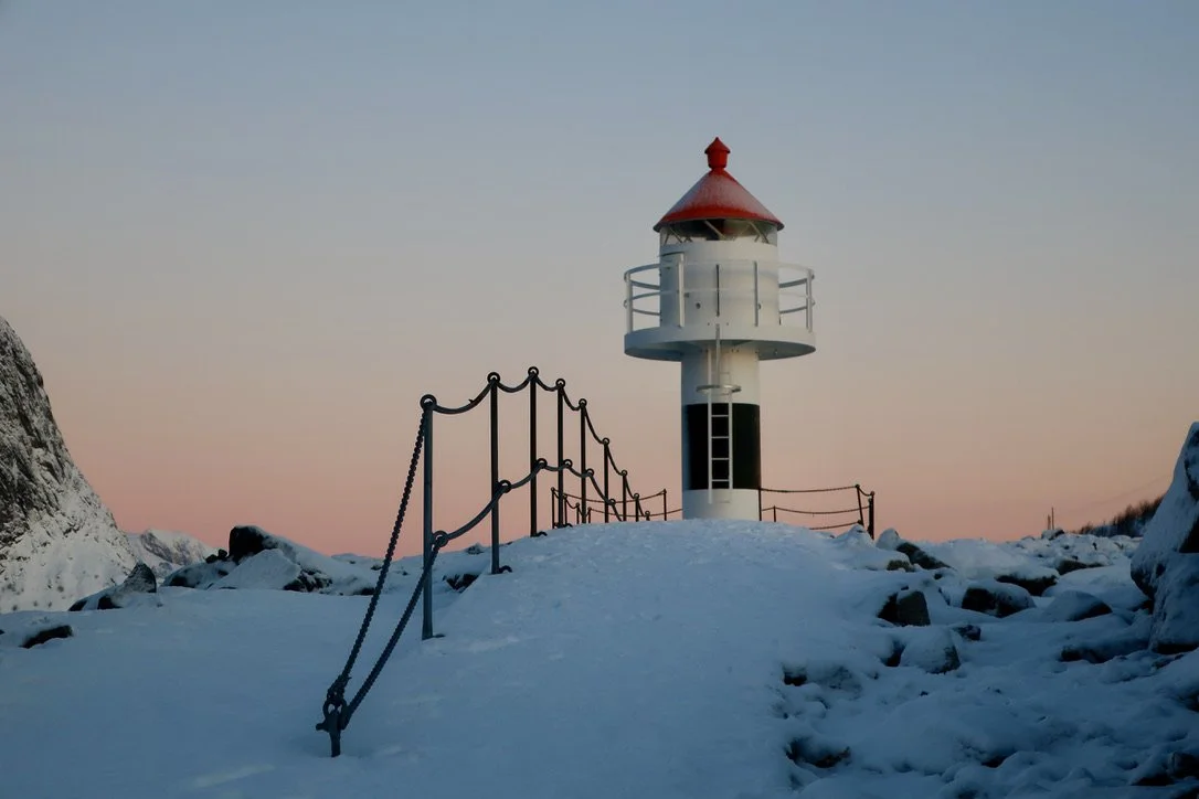 Reine, Norvège. Phare blanc avec toit rouge sur une falaise enneigée au coucher du soleil - Photographe voyage à La Réunion