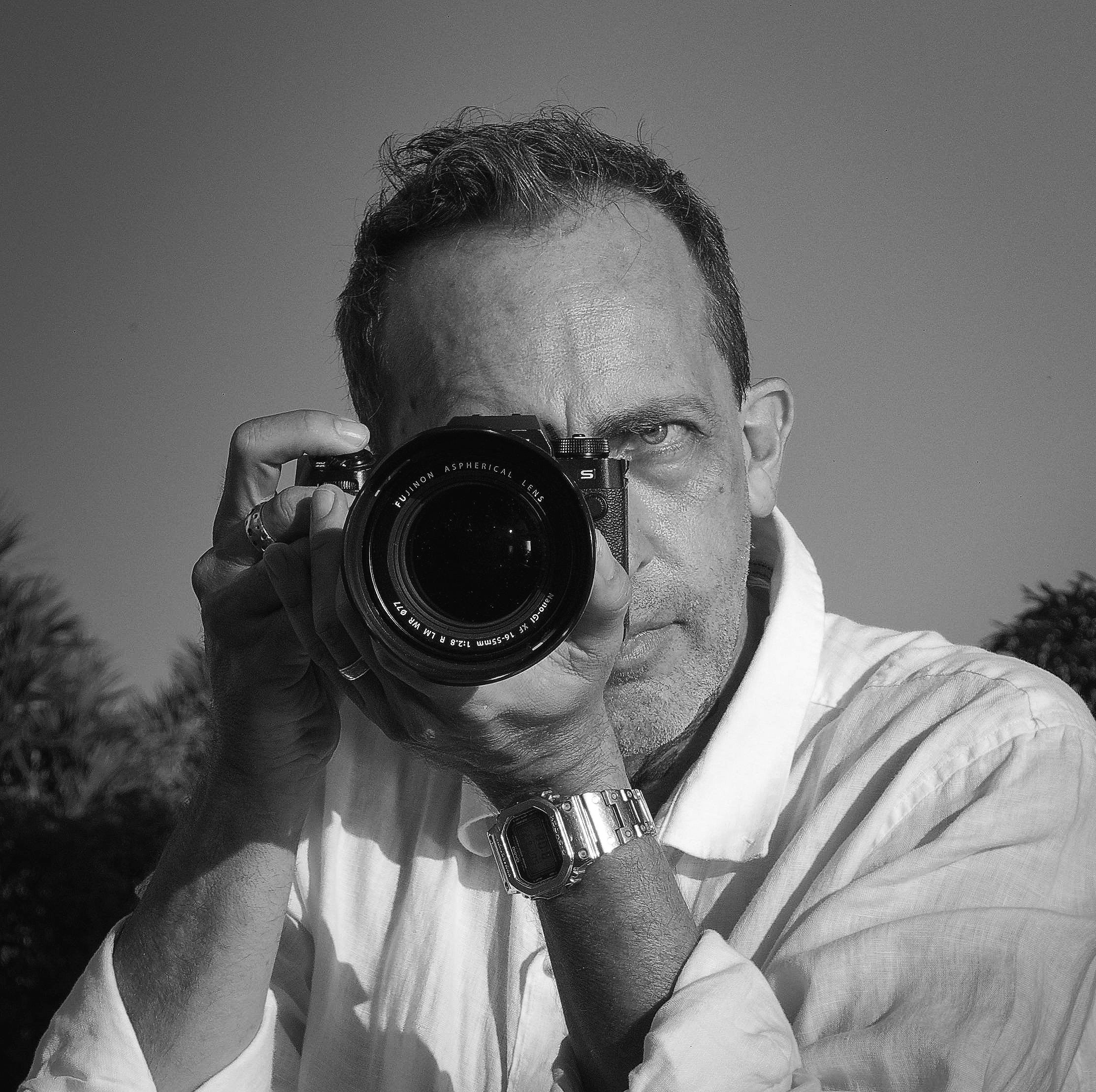 Stéphane Nicolas Dujardin, photographe avec son appareil photo, regardant à travers le viseur, en noir et blanc.