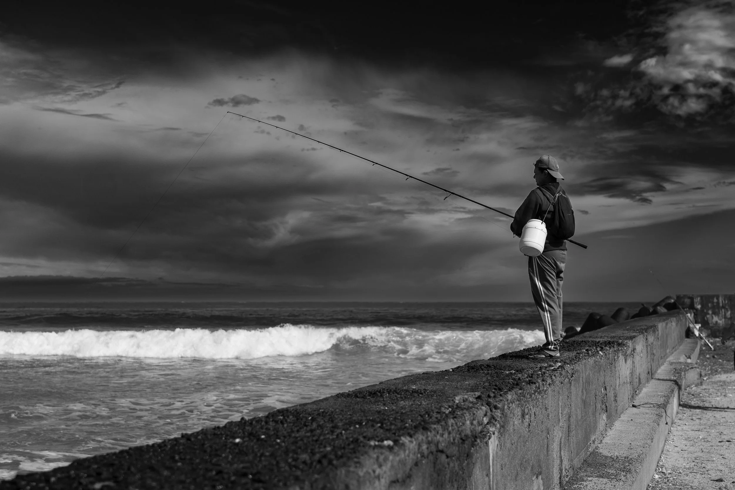 Pêcheur en noir et blanc sur une digue face à l’océan — Photographe lifestyle à La Réunion