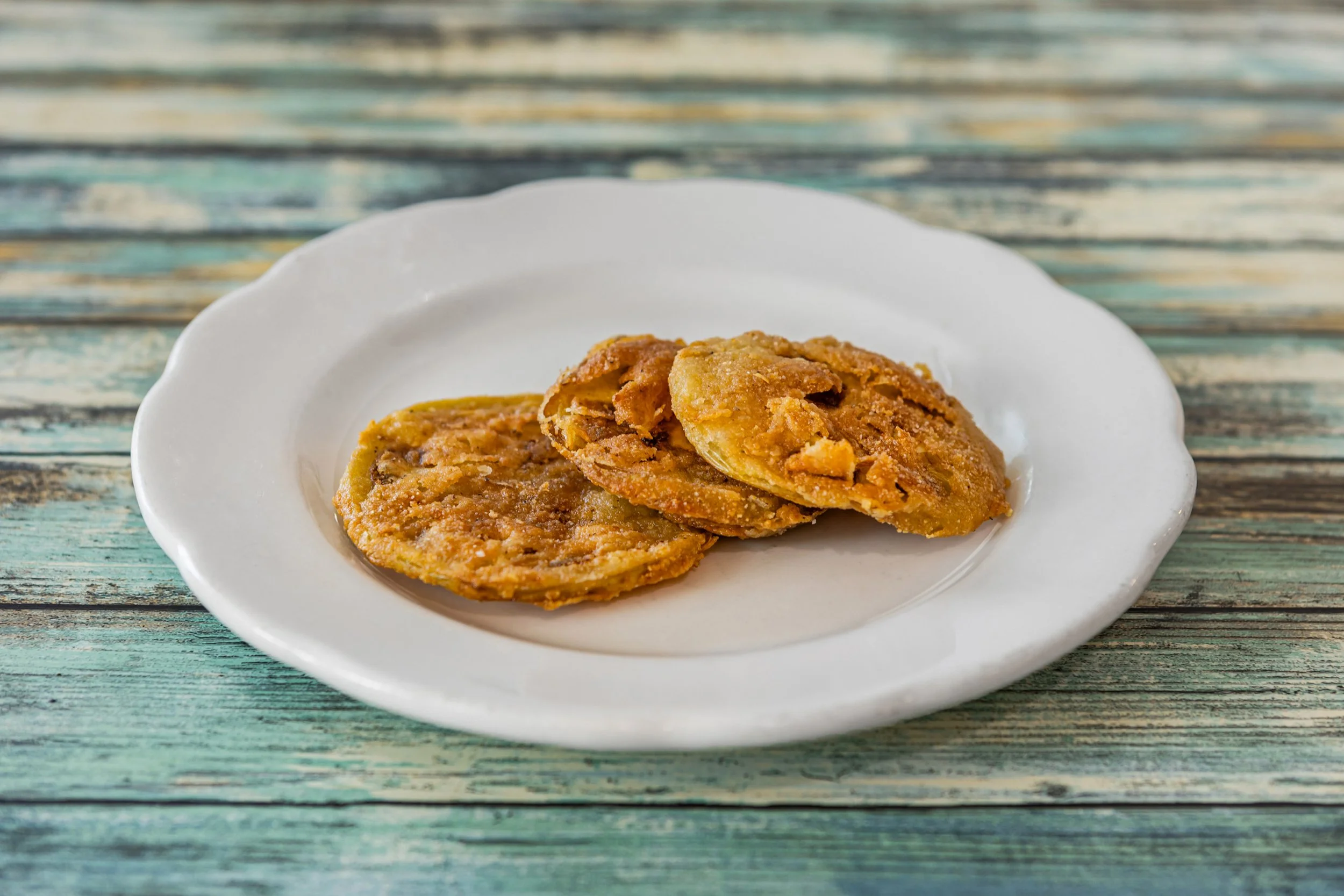 Three fried plantains on a white plate, placed on a rustic wooden table.