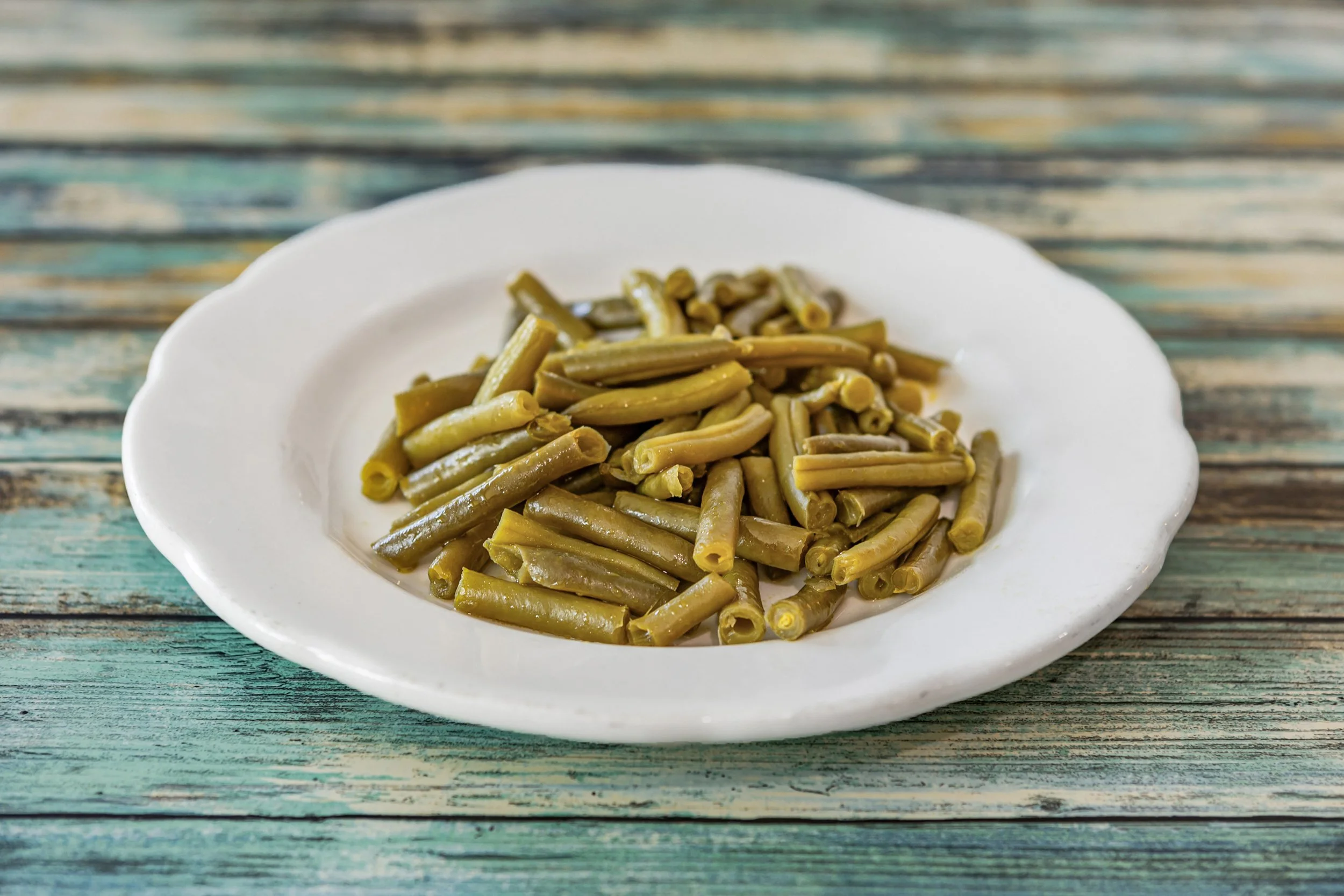 Cooked green beans on a white plate set on a rustic wooden surface.