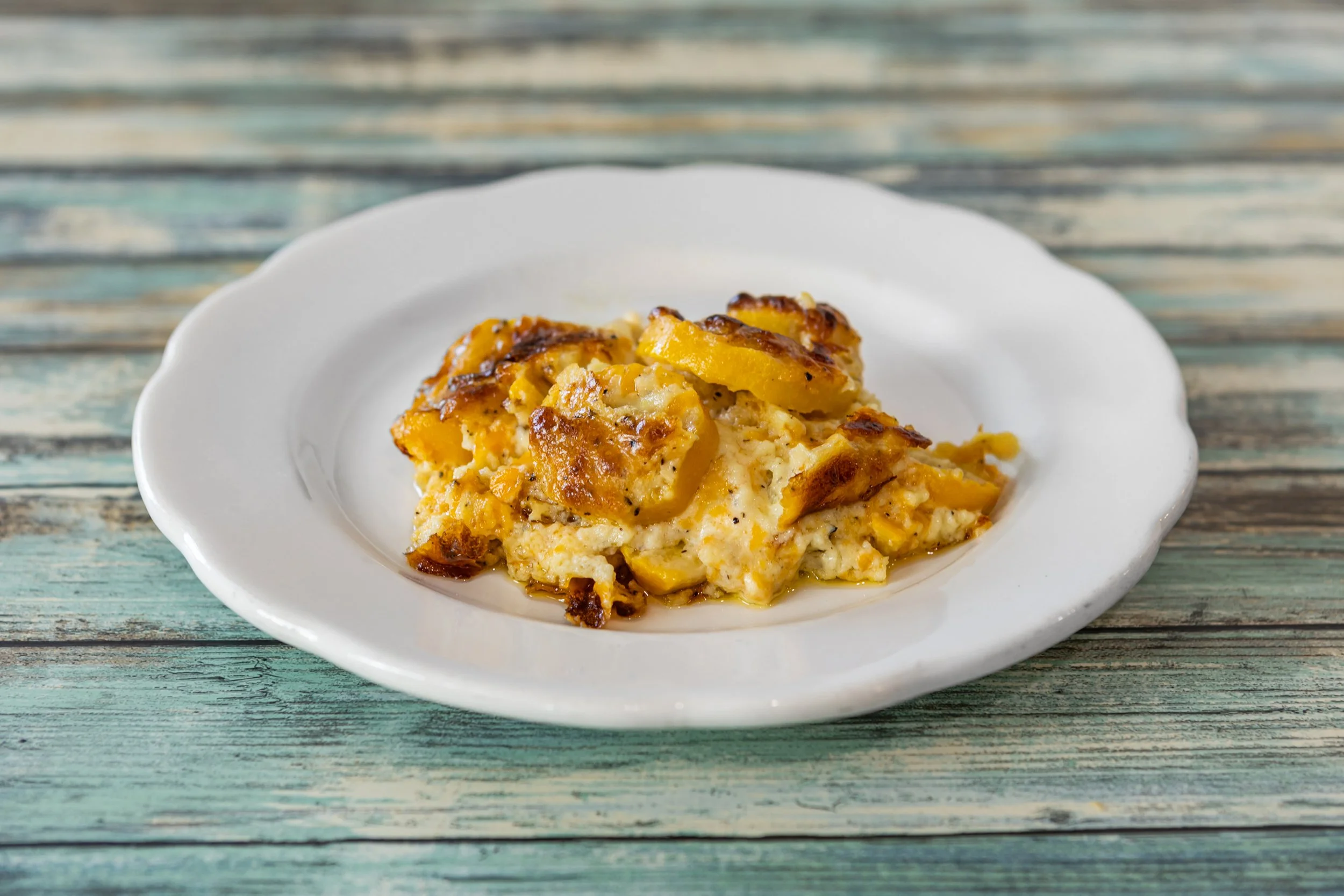 A serving of baked scrambled eggs with potatoes on a white scalloped plate, placed on a rustic wooden table.