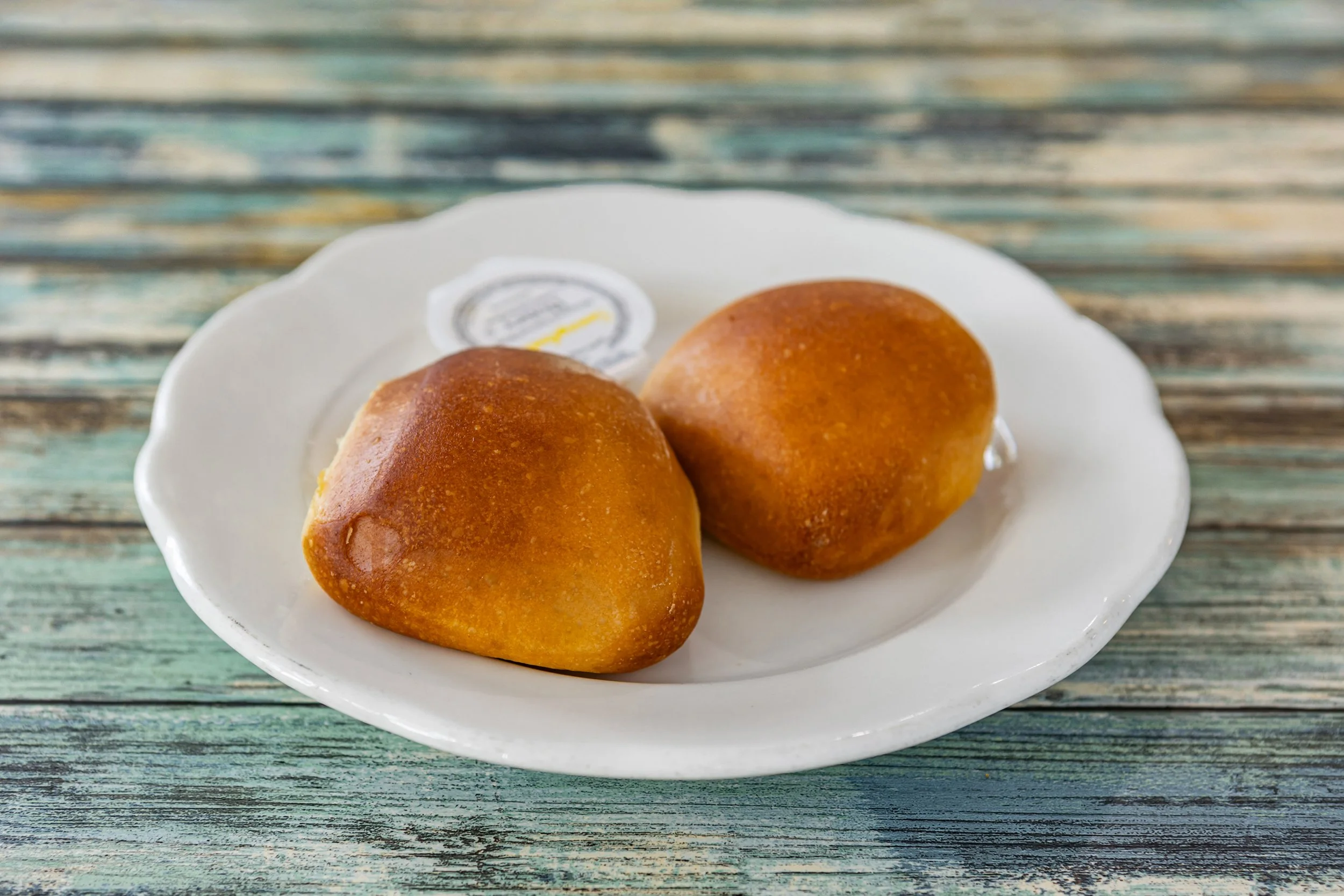 Two golden-brown fried dough balls on a white scalloped-edged plate on a rustic wooden surface.