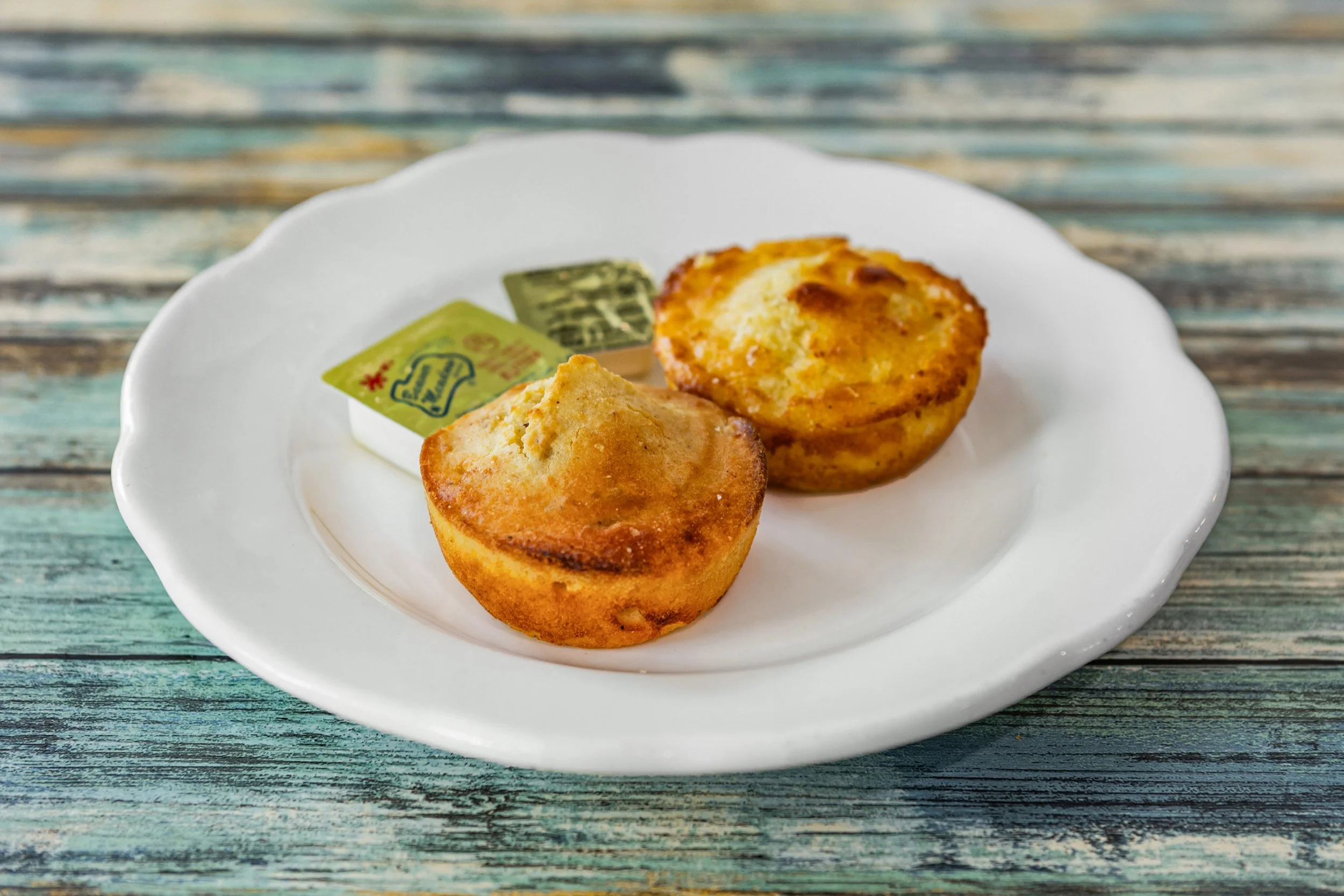 Two muffins served on a white plate with butter and jam, on a rustic wooden table.
