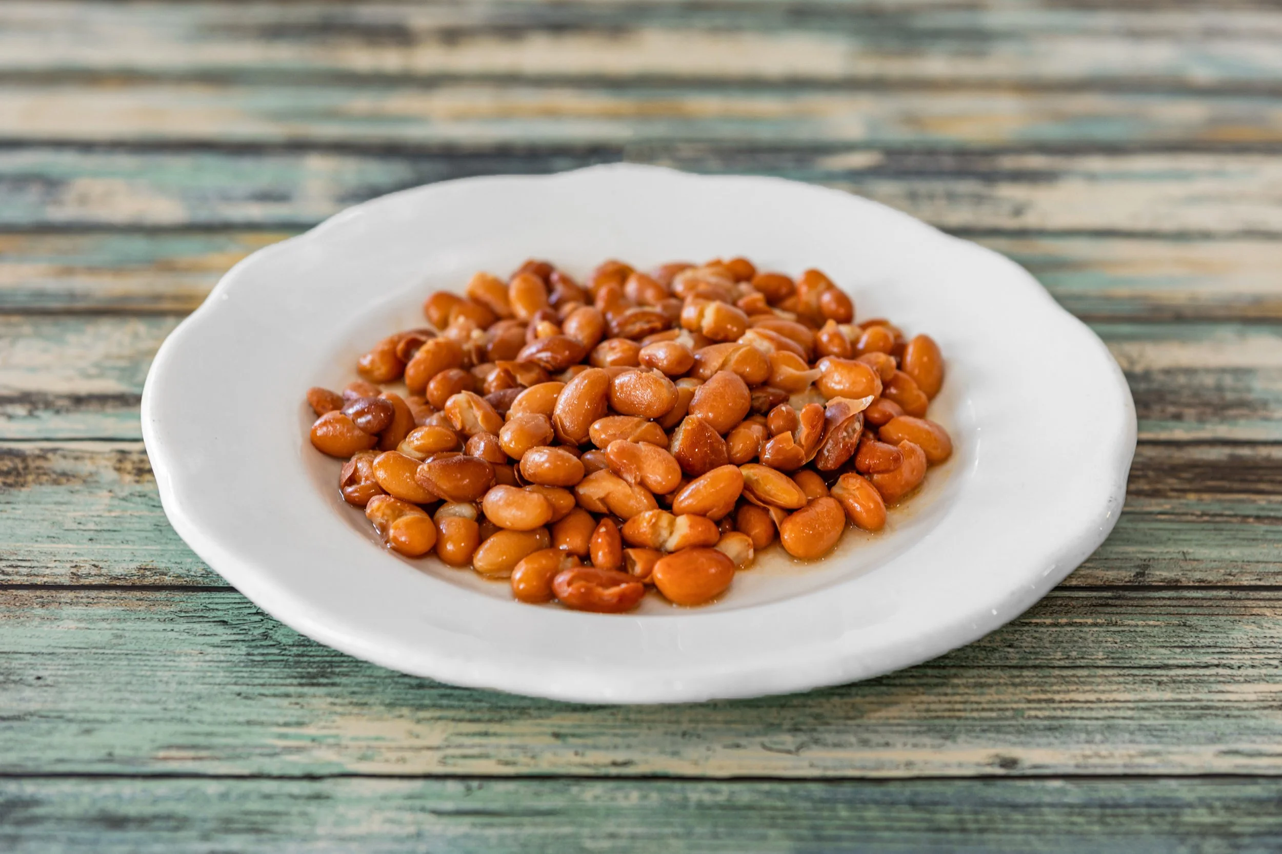 Cooked pinto beans on a white plate with a rustic wooden surface background.