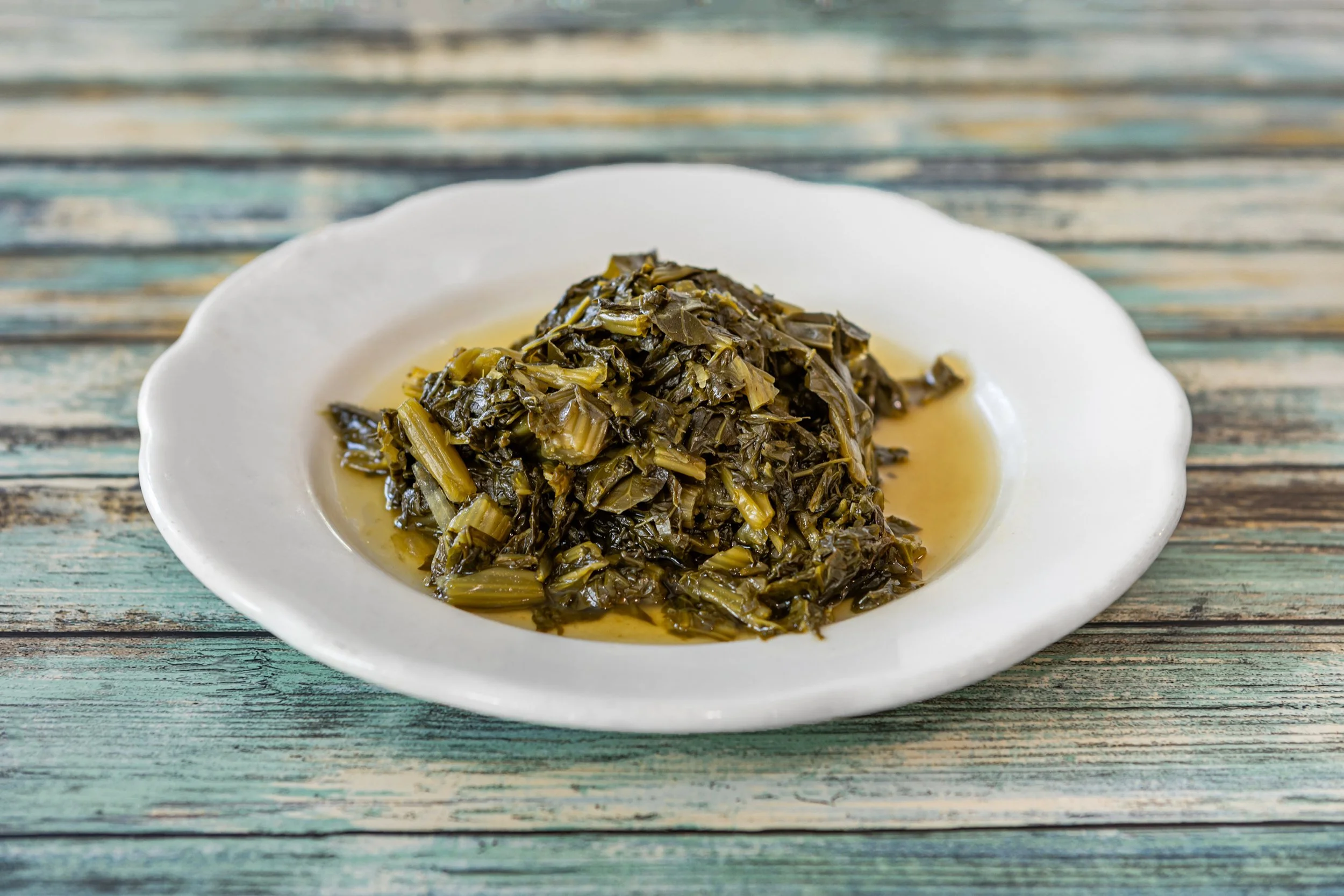 Stewed collard greens on a white plate on a rustic wooden table.