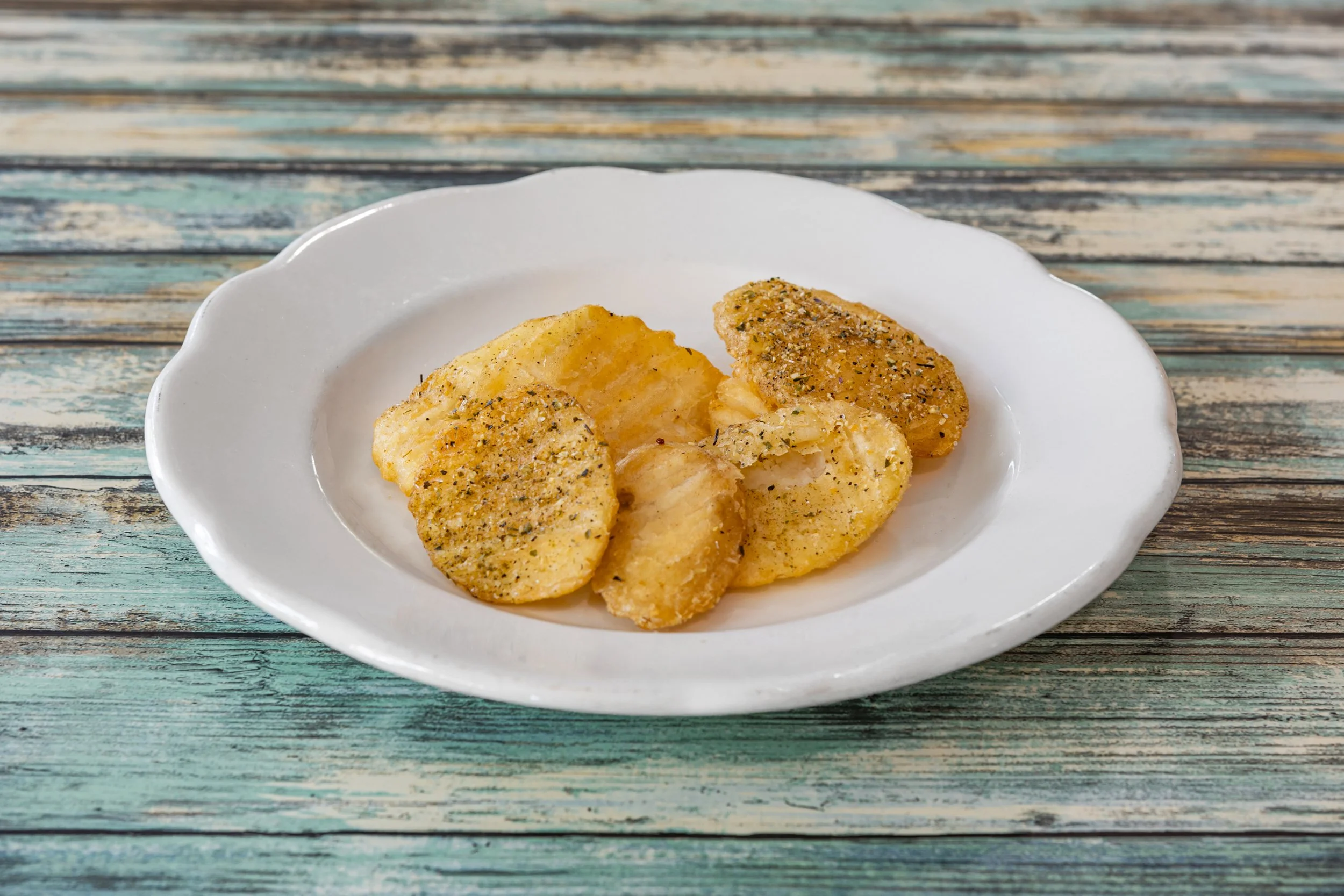 Plate of seasoned potato slices on a white dish, set on a rustic wooden surface.