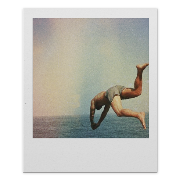 A person performing a handstand in mid-air over the ocean, with one leg bent and the other extended, in front of a clear sky.