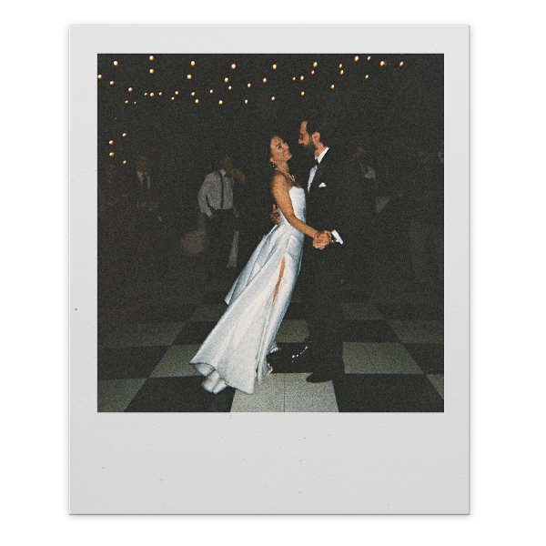 A bride and groom dancing at their wedding reception in a dimly lit venue with string lights overhead.